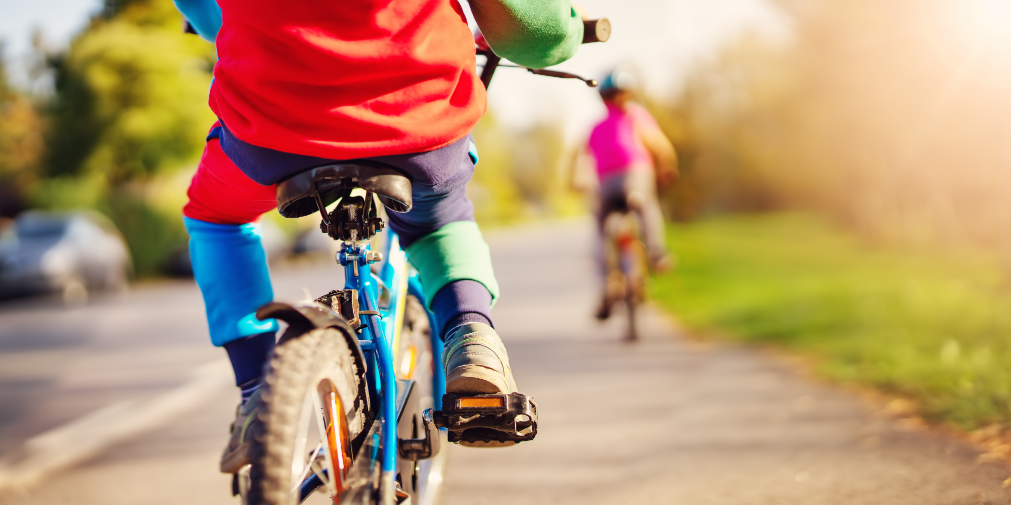 Zwei Kinder fahren mit Fahrrädern auf einem Weg, umgeben von Bäumen und Sonnenlicht.
