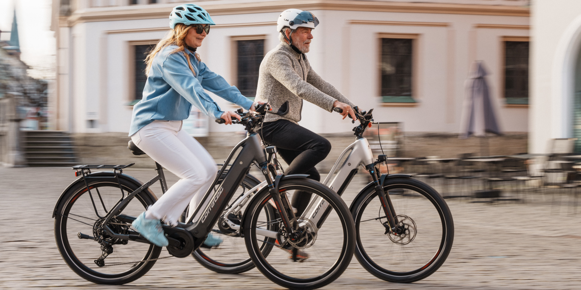 Zwei Personen fahren nebeneinander auf E-Bikes in einer Stadtstraße.