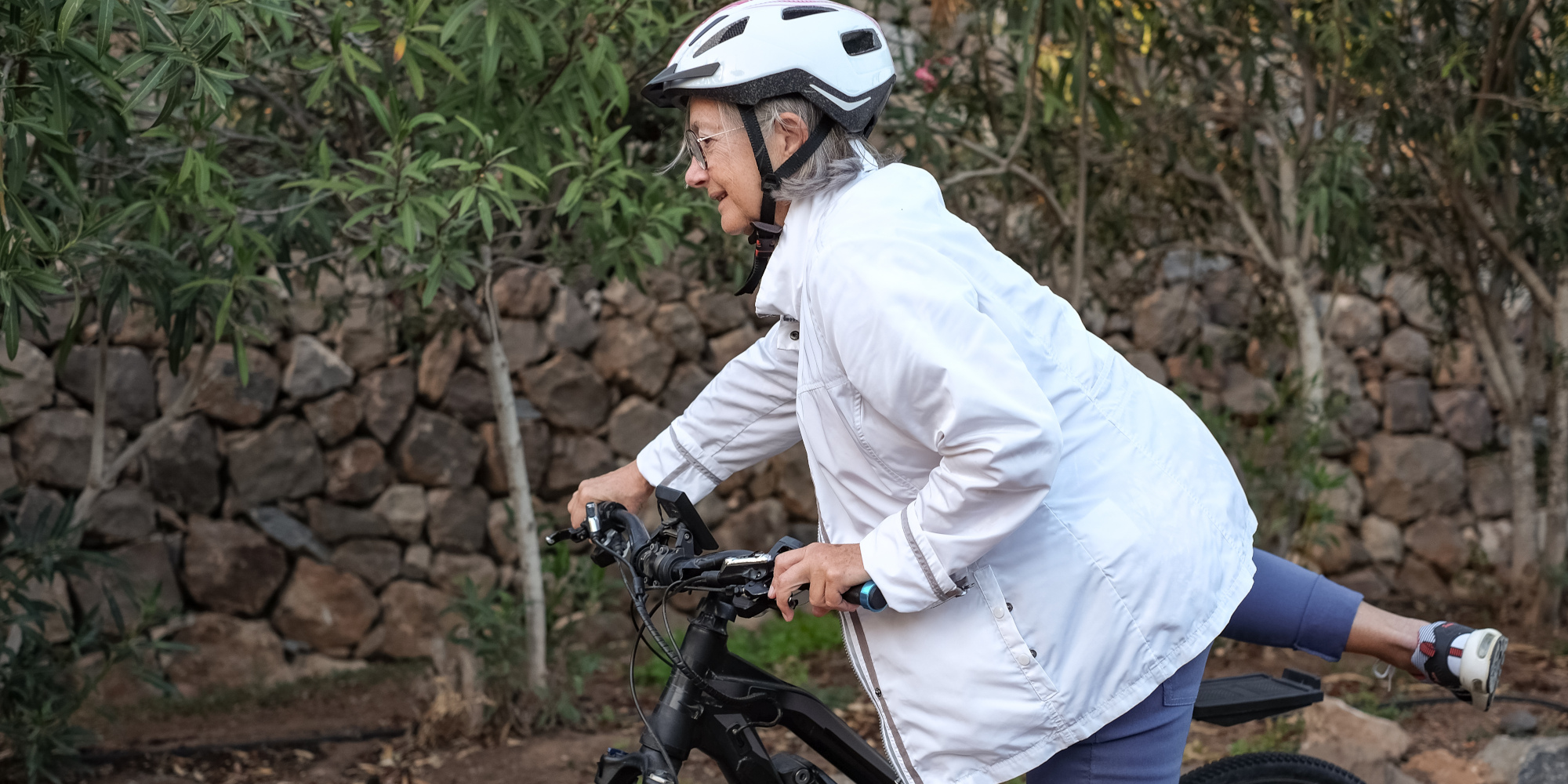 Eine Person in weißer Jacke und Helm fährt auf einem Fahrrad in der Natur.
