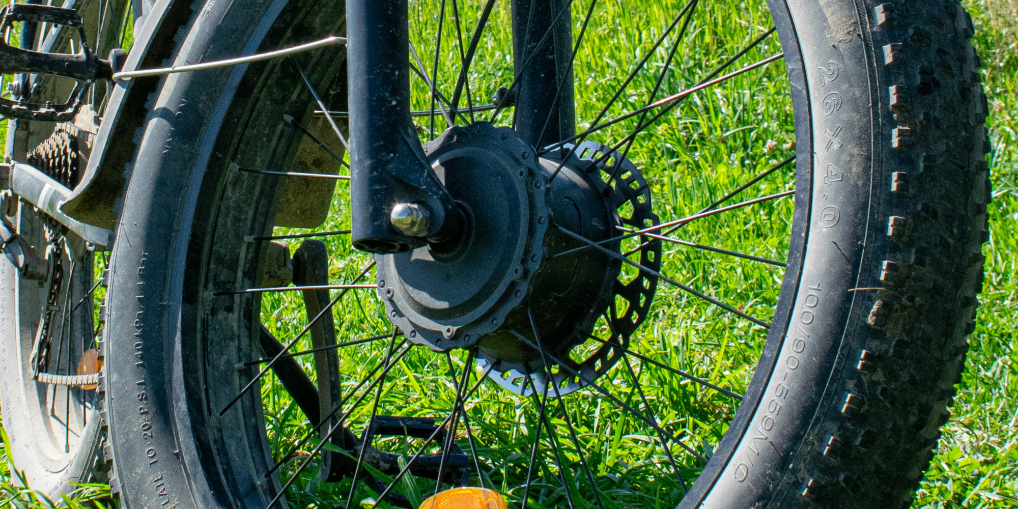 Vorderteil eines Fahrrads mit einem elektrischen Motor, grüne Wiese im Hintergrund.