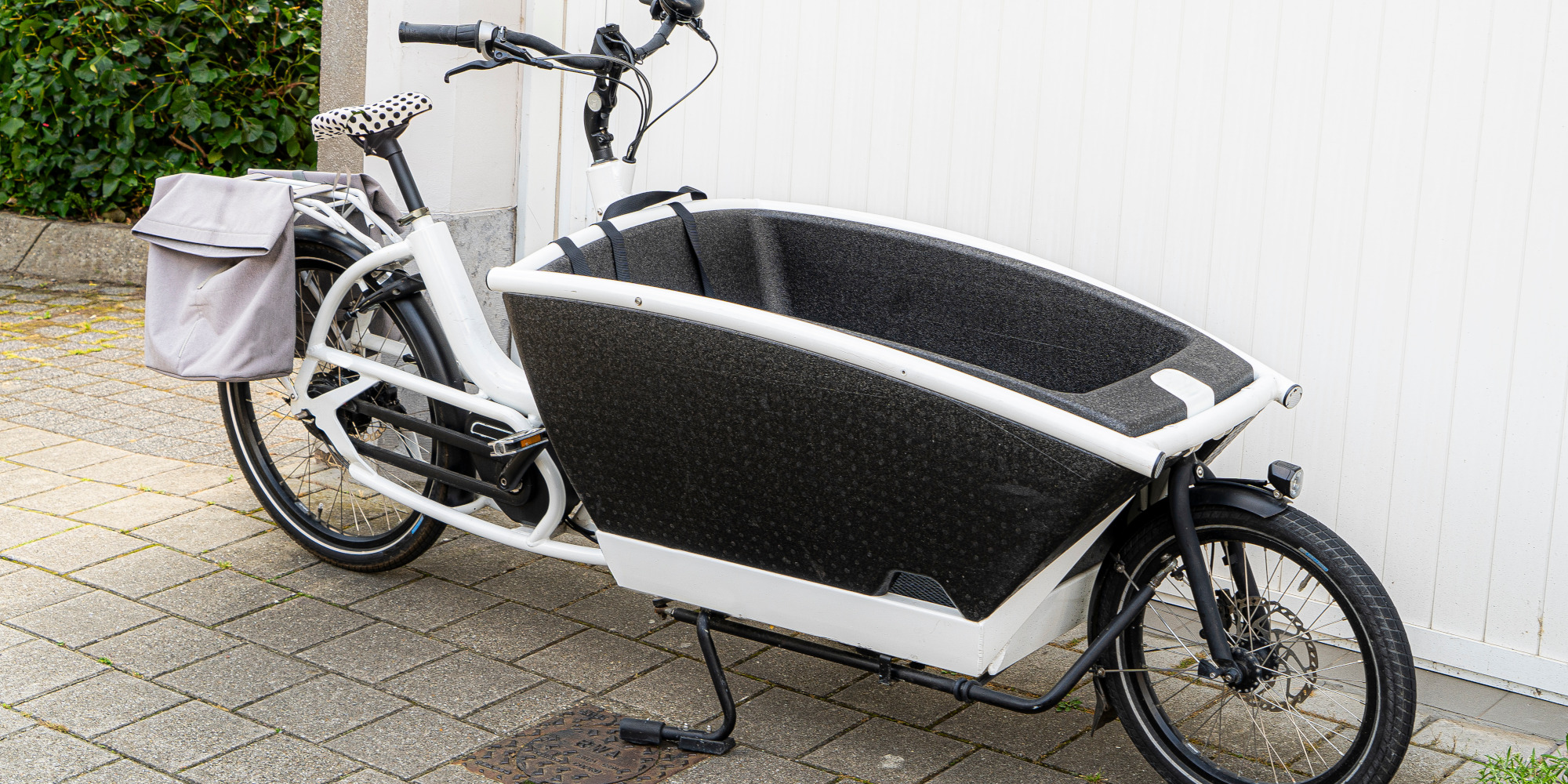 Lastenrad mit einem großen, schwarzen Transportbereich und einer grauen Tasche.
