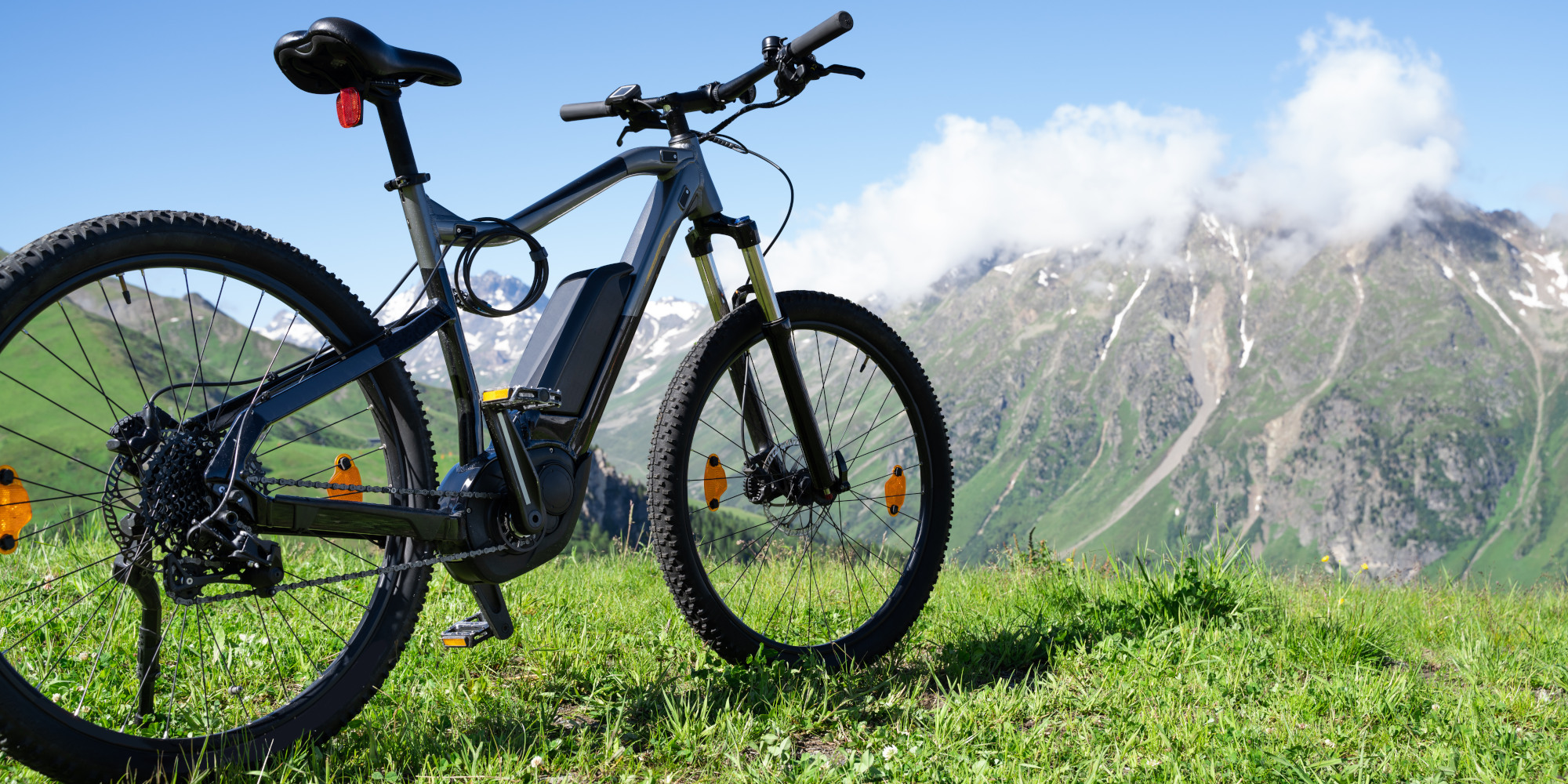 Ein Fahrrad steht auf grünem Gras mit Bergen im Hintergrund und blauen Himmel.