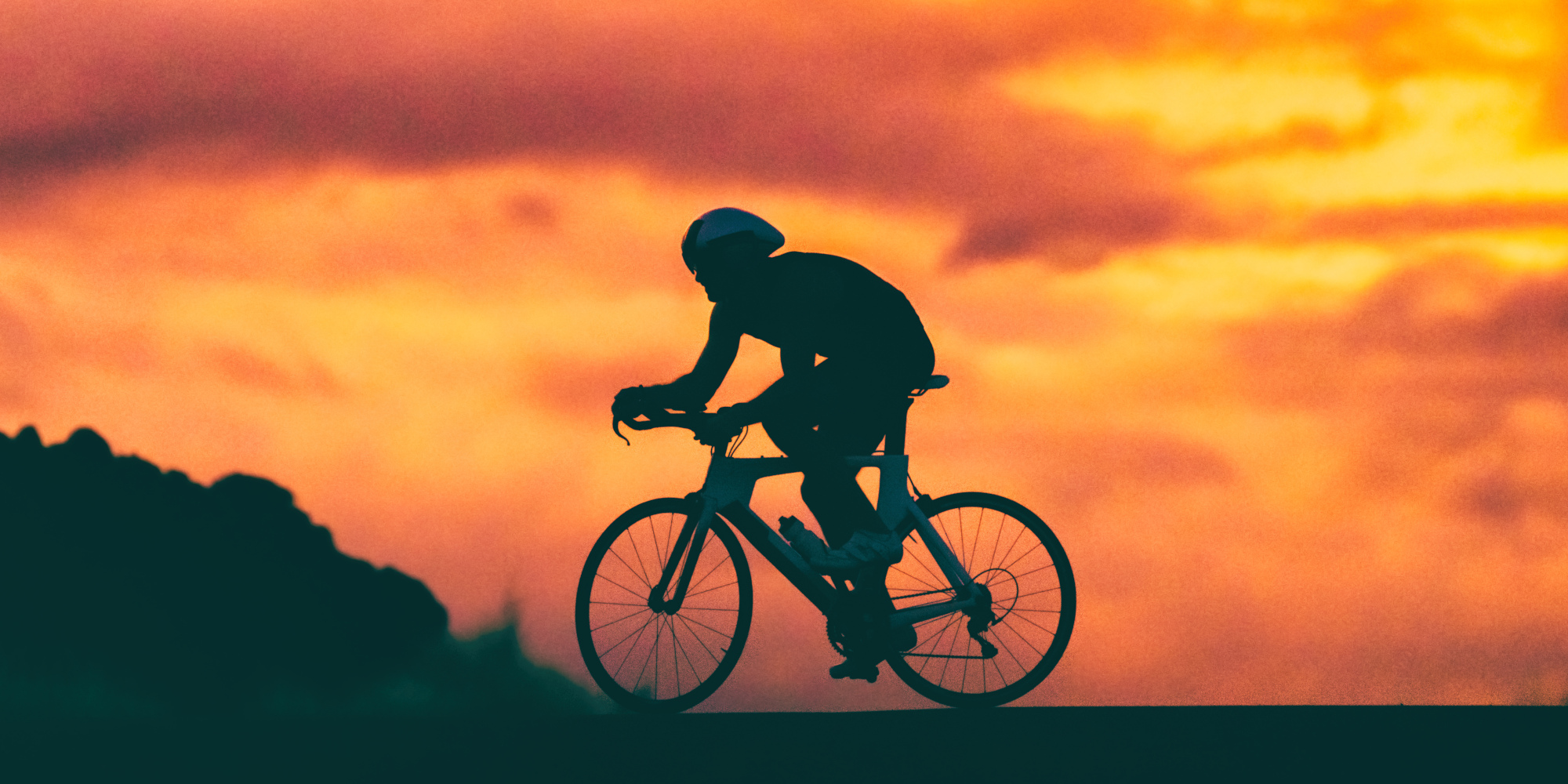 Radfahrer in Silhouette gegen einen bunten Sonnenuntergang.