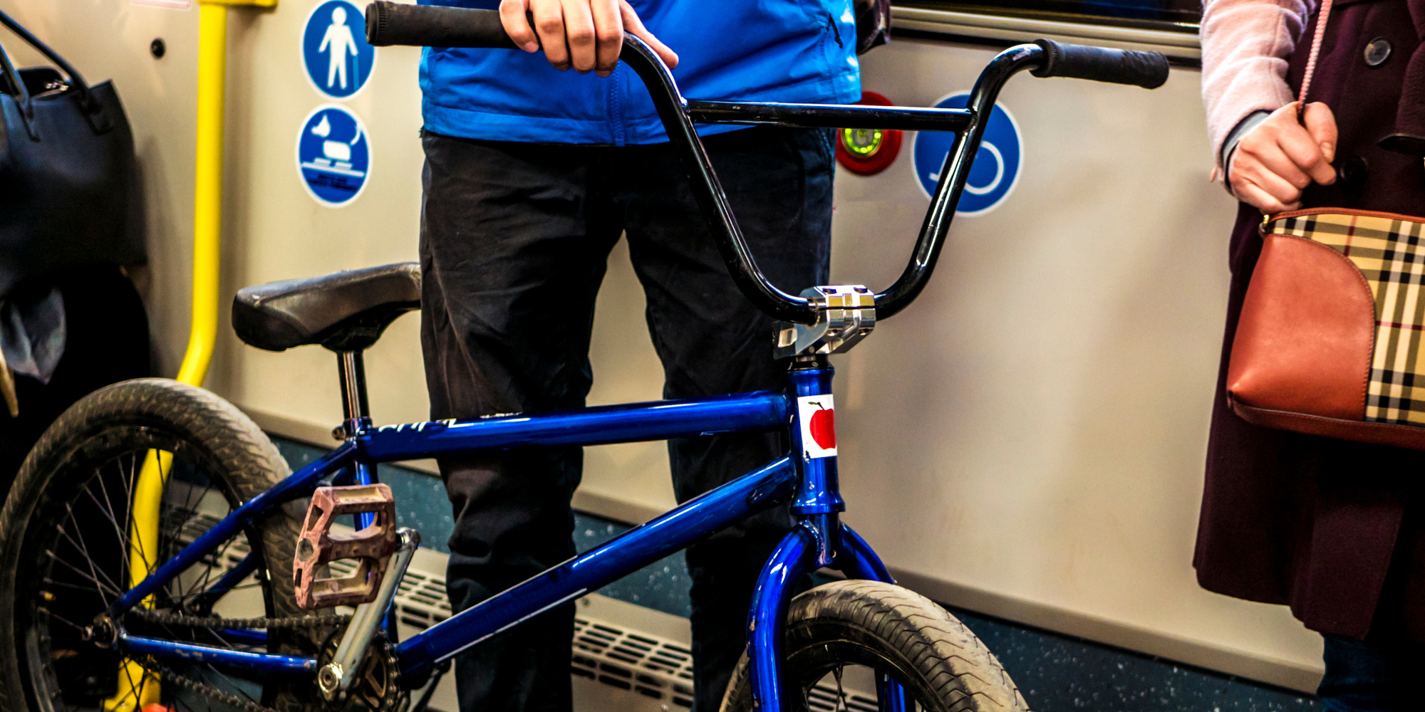 Junger Mann hält ein BMX-Fahrrad in der U-Bahn, neben einer Person mit Handtasche.