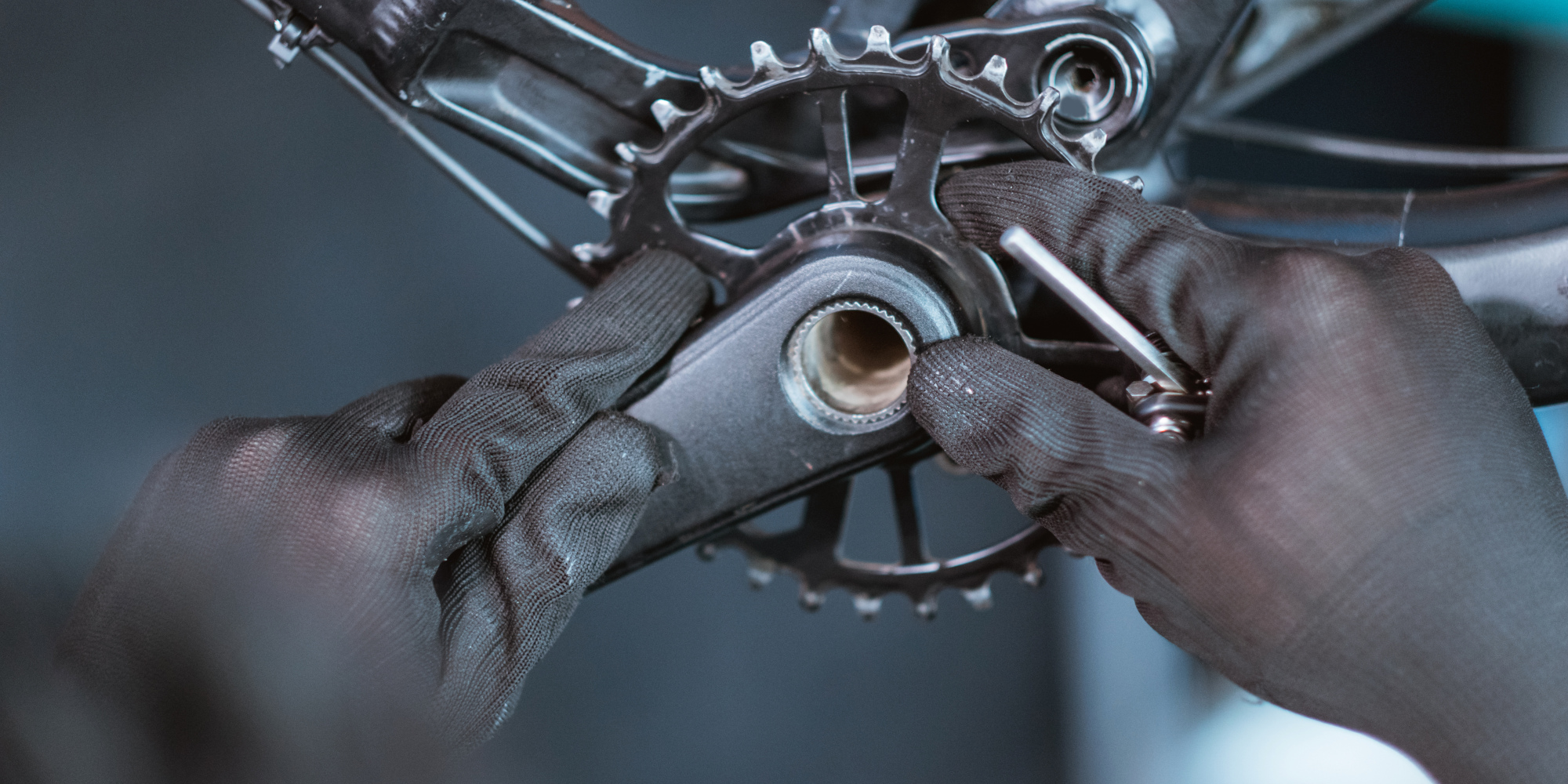 Tretlager wechseln Hände in schwarzen Handschuhen montieren eine Fahrradkurbel.