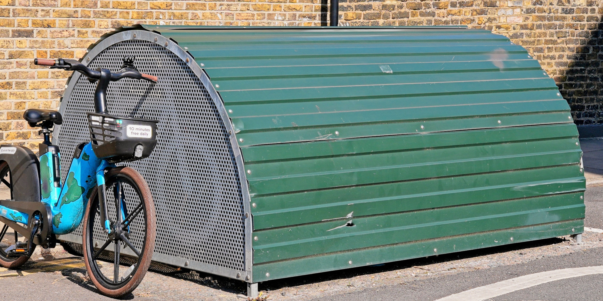 Grüne Fahrradunterstand mit einem blauen Fahrrad daneben.