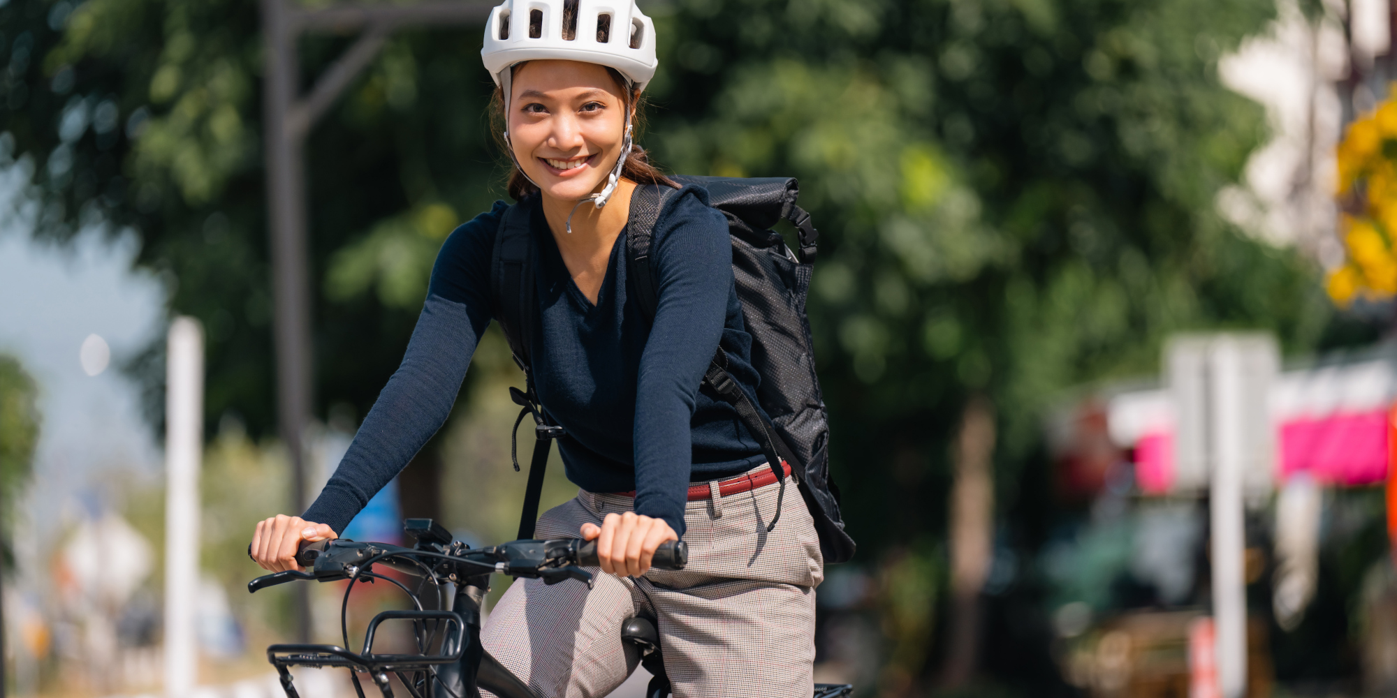 Radfahrer mit Rucksack auf einem sonnigen Weg, umgeben von Bäumen.