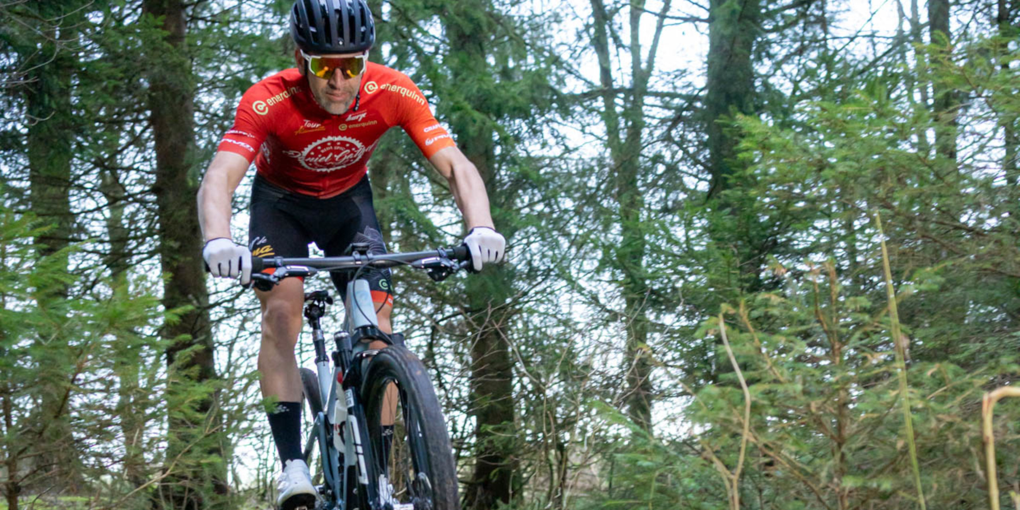 Ein Mountainbiker in rotem Trikot fährt auf einem Waldweg.