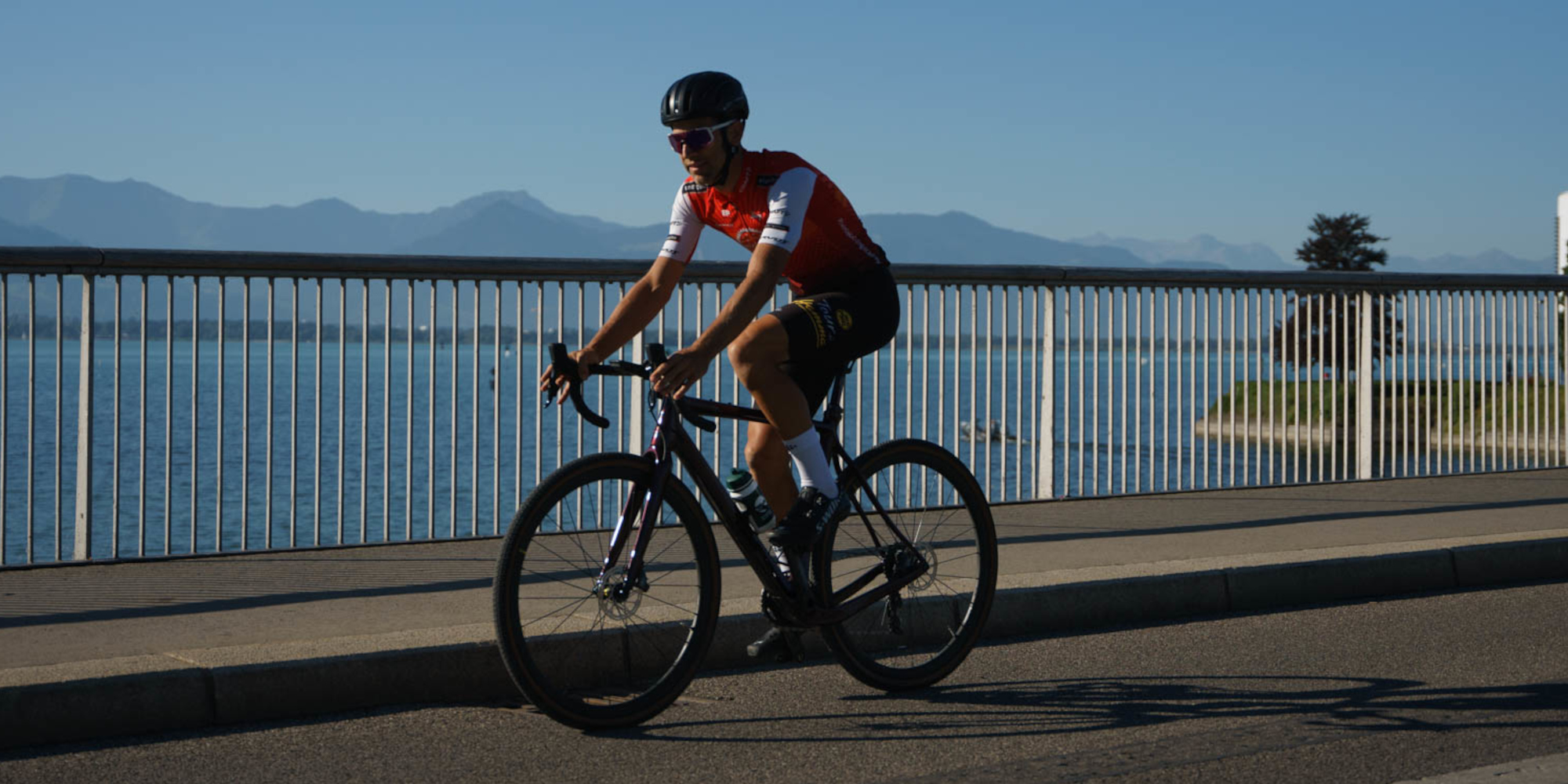 Radfahrer in Rot und Schwarz fährt an einer Küstenpromenade vorbei.