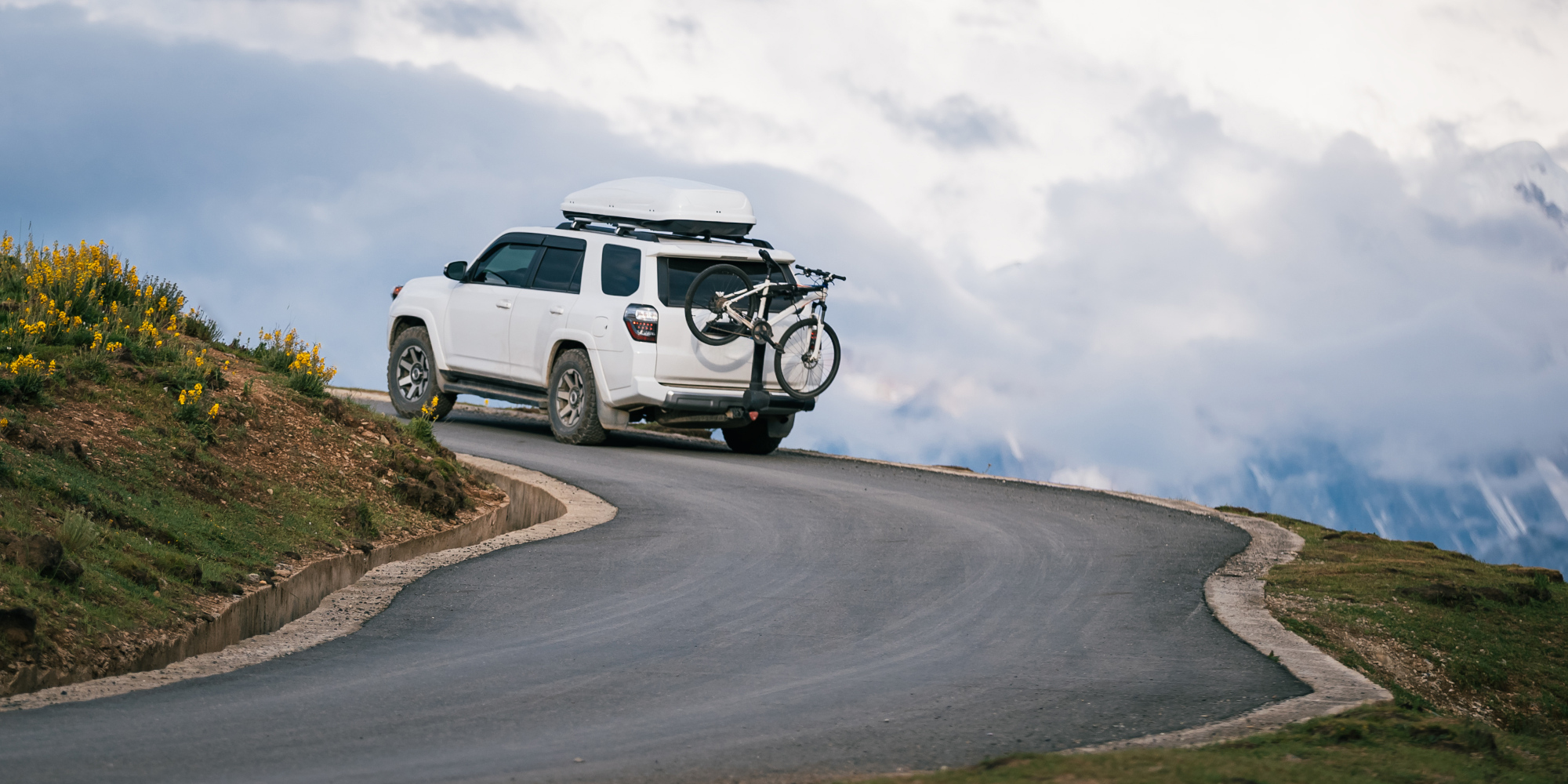 Ein weißes SUV fährt um eine kurvige Straße mit Bergen im Hintergrund.