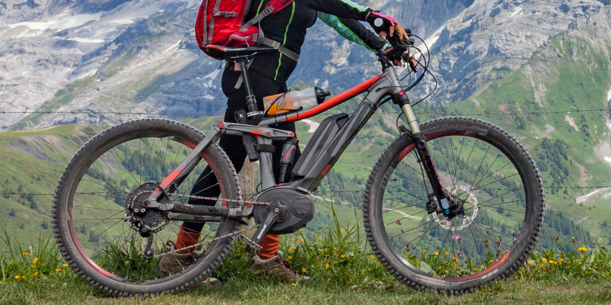 Eine Person steht neben einem Elektro-Mountainbike in einer bergigen Landschaft.