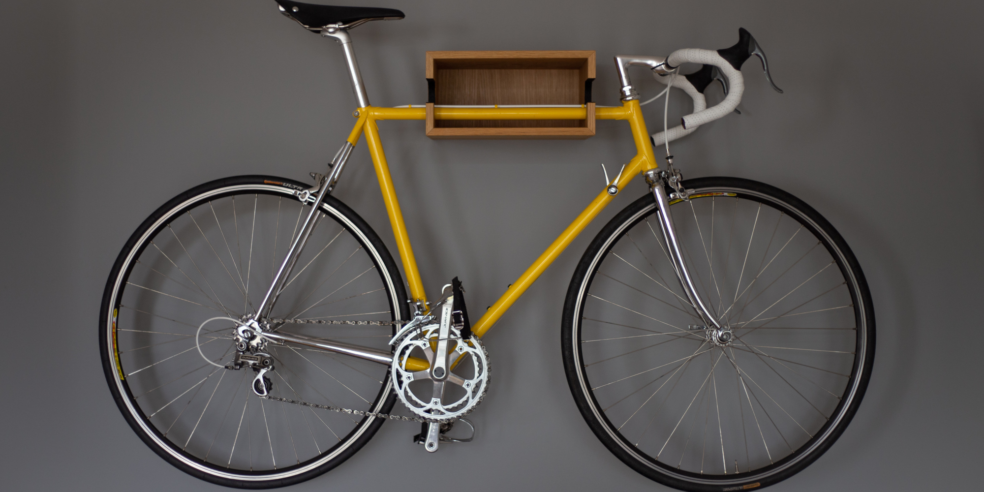 Gelbes Rennrad mit silbernen Elementen, an grauer Wand montiert.