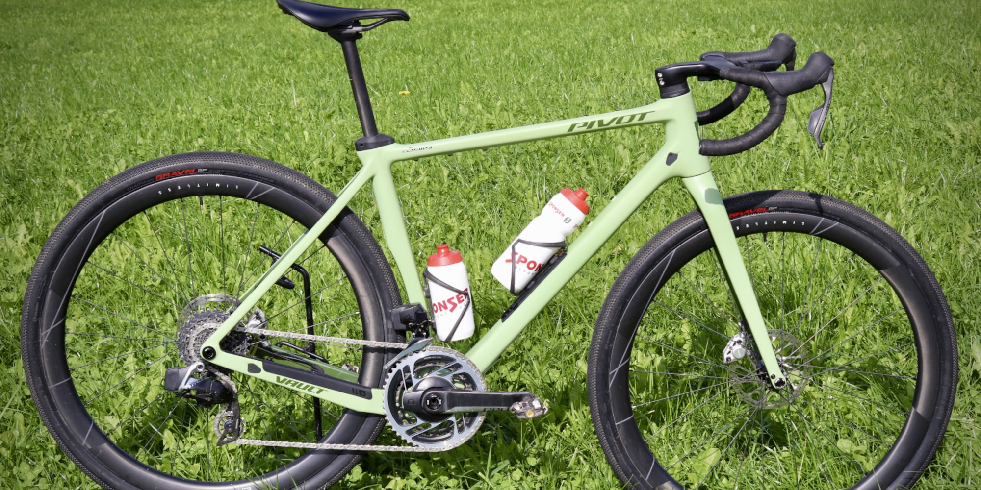 Grünes Gravelbike mit zwei Trinkflaschen auf saftigem, grünem Gras.