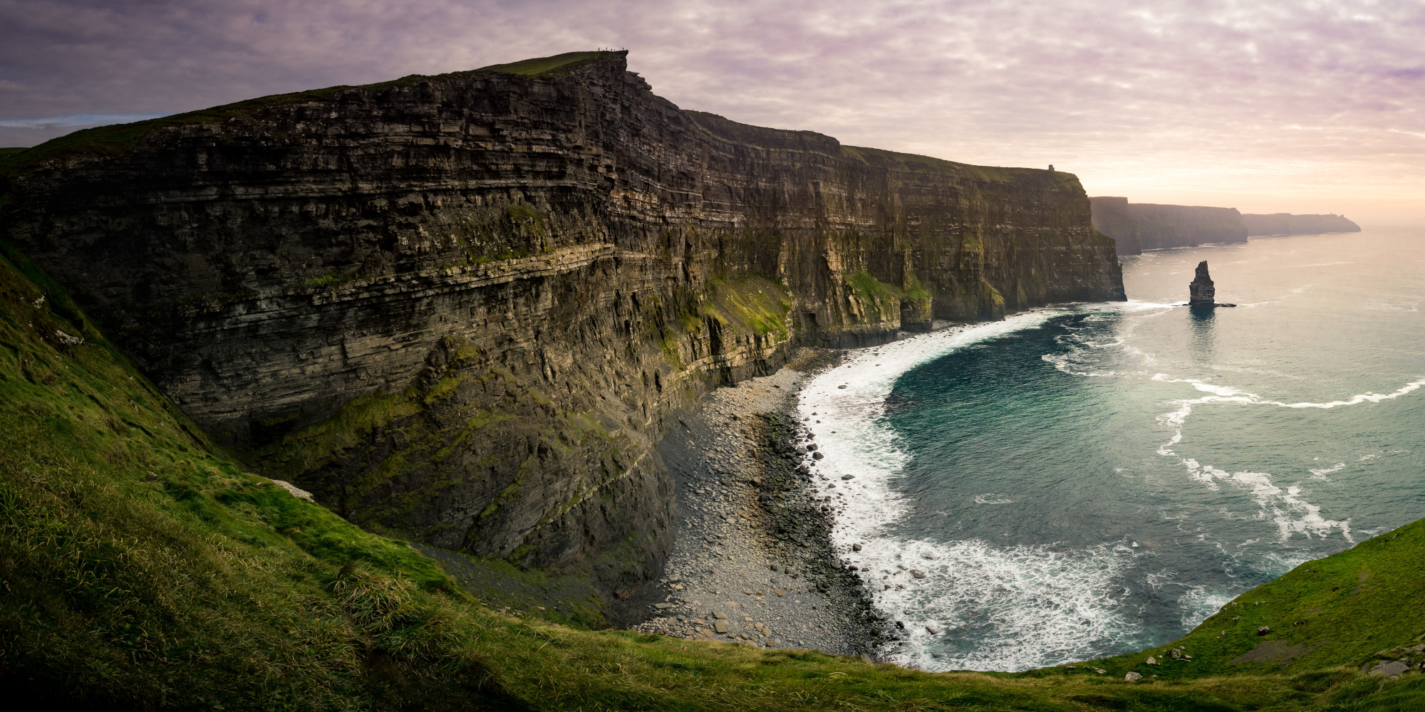 Hohe Klippen über dem ruhigen, blauen Wasser mit sanften Wellen und grauem Himmel.