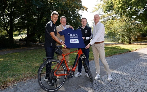 Vier Personen stehen im Freien und halten ein T-Shirt vor einem Fahrrad.