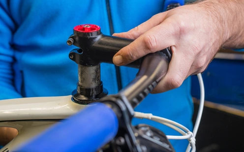 Lenkerhöhe einstellen Hände montieren den Lenker an einem Fahrradrahmen in einer Werkstatt.