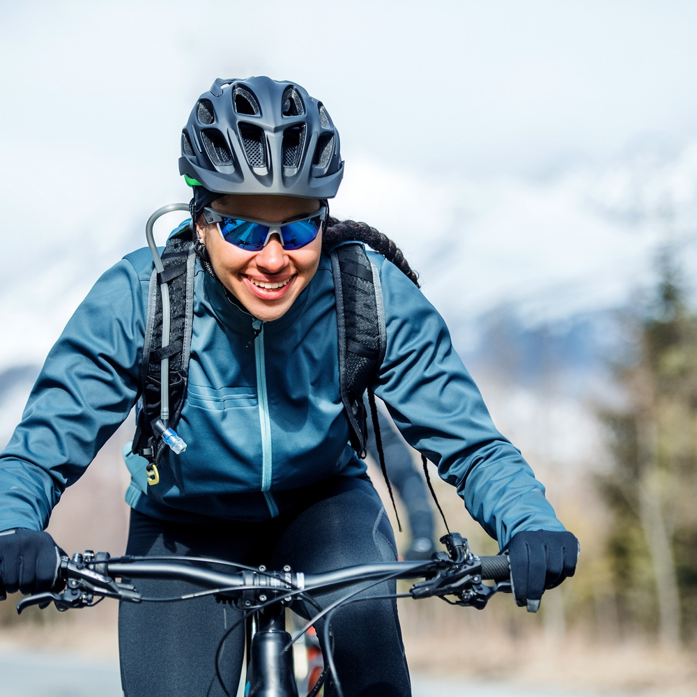 Radfahren im Winter macht Spaß - wenn nicht gerade akute Glatteisgefahr besteht. Frontale Ansicht einer lächelnden Fahrradfahrerin in Winterkleidung