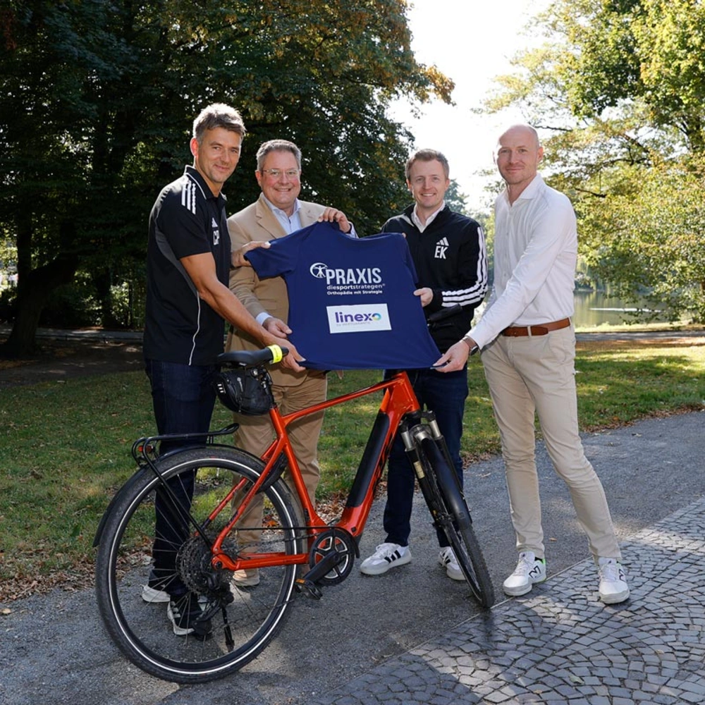 Vertreter von linexo und den Recken halten ein T-Shirt vor einem Fahrrad in einem Park.