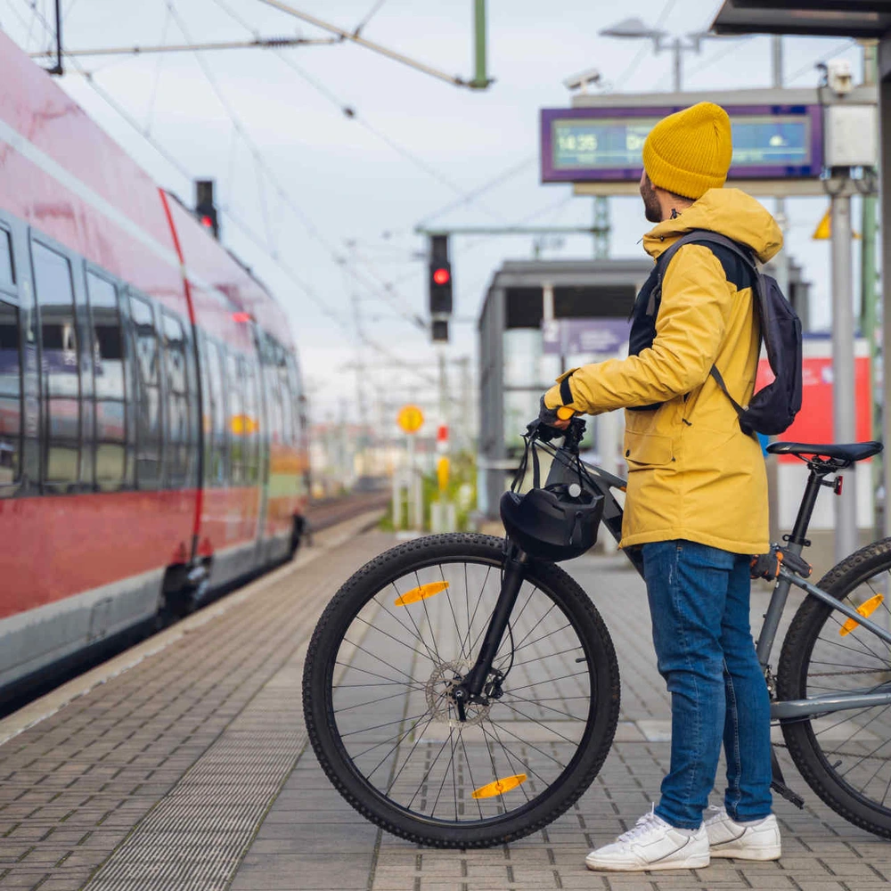 Mann in gelber Jacke wartet mit seinem Fahrrad auf den Zug