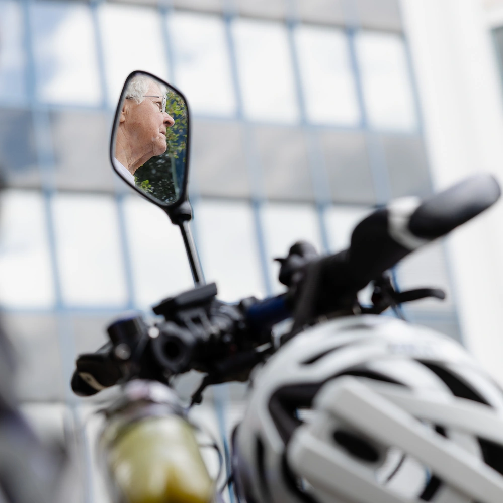 Fahrradrückspiegel mit reflektierenden Fenstern und einem weißen Helm im Hintergrund.