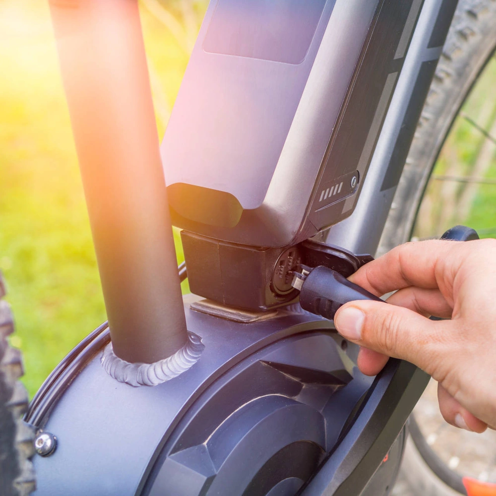 Person verbindet ein Kabel mit dem Akku 750 h eines E-Bikes, um diesen zu laden