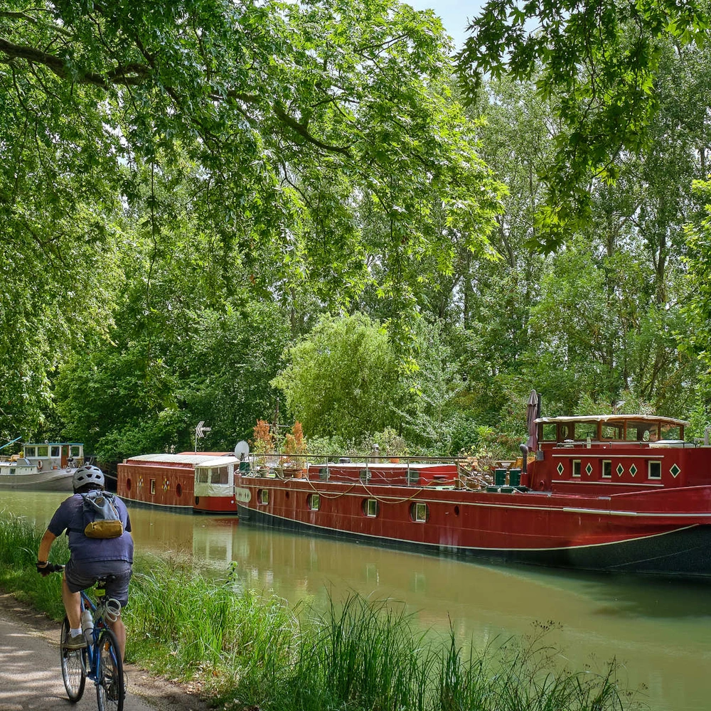 Radfahrer fährt am Canal du Midi in Frankreich entlang, auf dem Boote liegen.