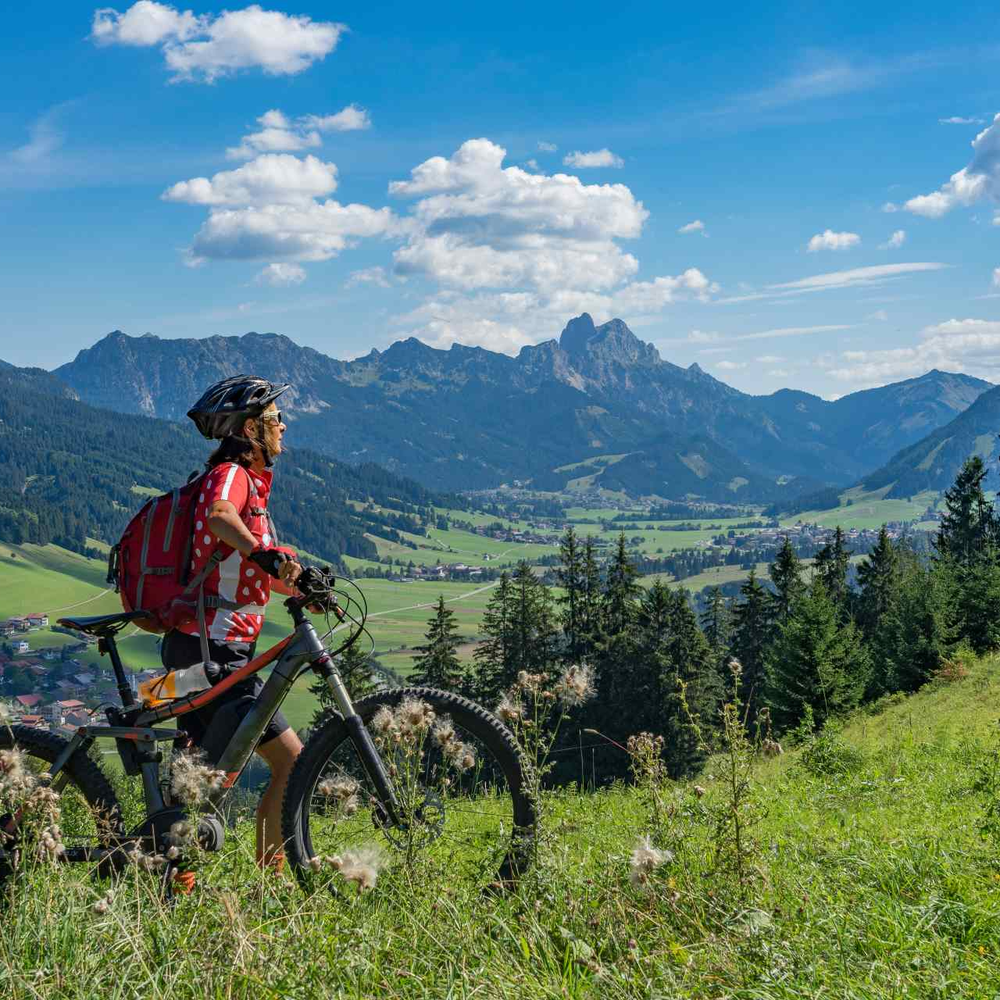 Ist das Light-E-MTB der neue Mega Trend 2024? Frau schiebt E-Mountainbike durch die Berge