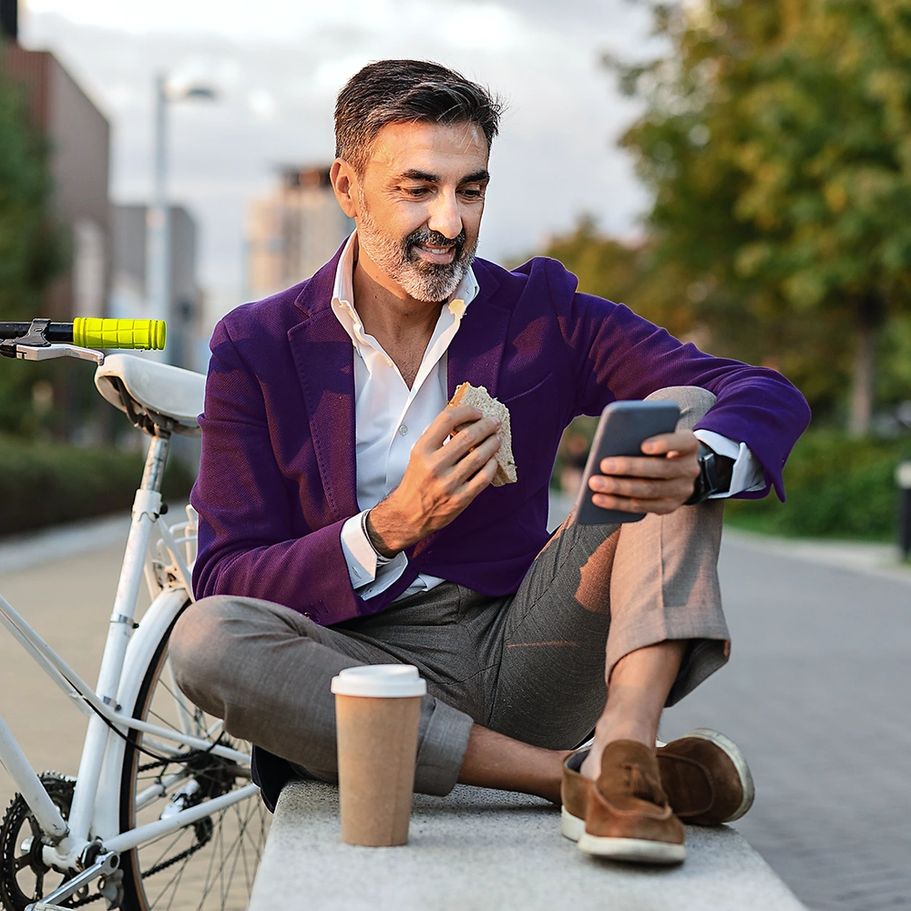Mann sitzt mit Smartphone und Kaffee auf einer Bank neben seinem Fahrrad