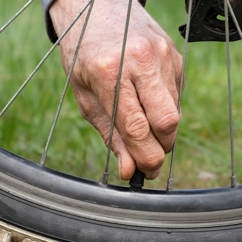 Nahaufnahme von einem Fahrradreifen mit einem Ventil, an dem eine Person anfässt.