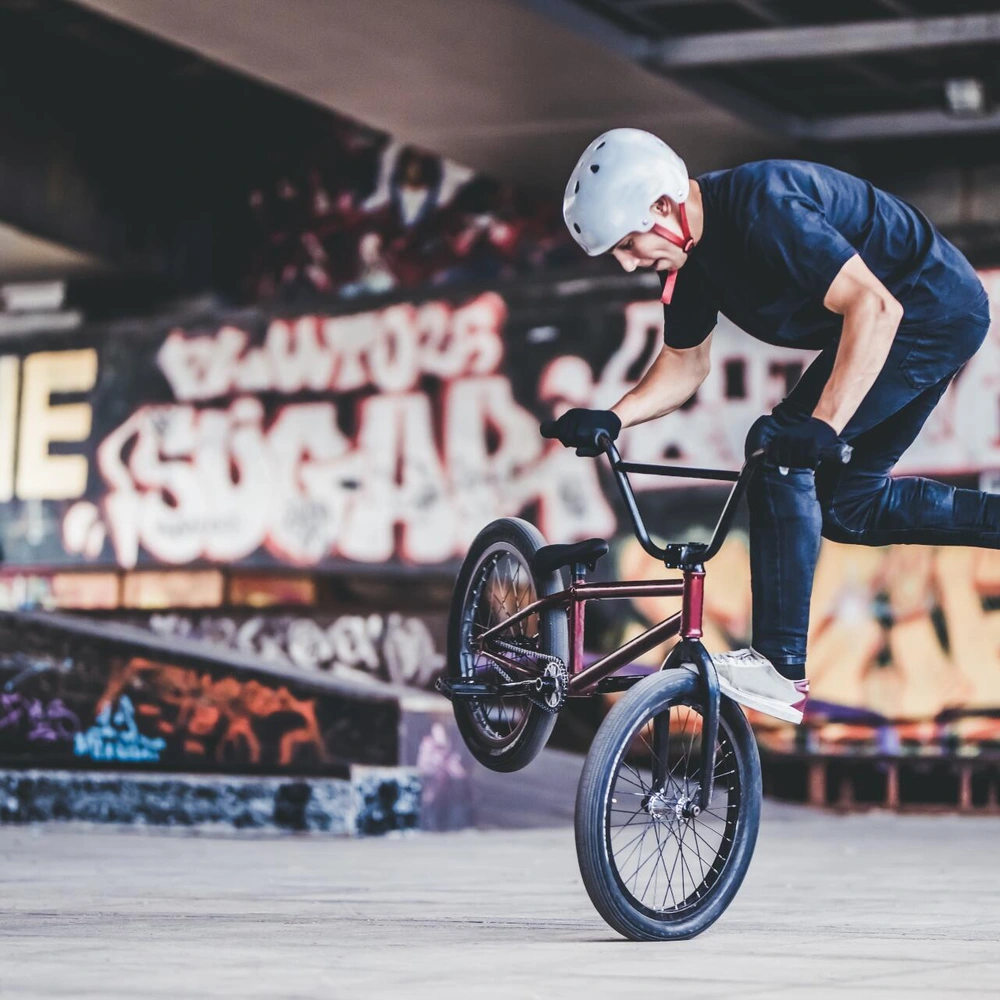BMX-Fahrer macht einen Trick in einem urbanen Skatepark mit buntem Graffiti
