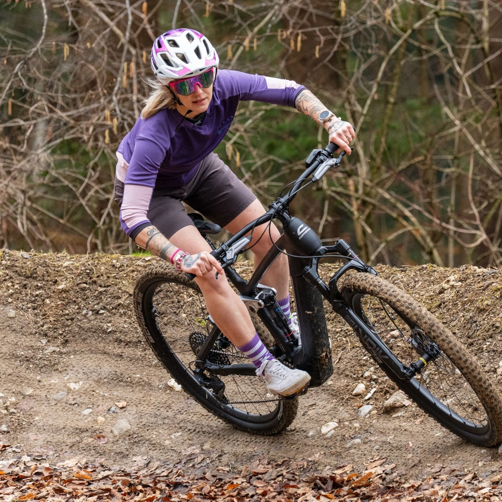 Mountainbikerin fährt mit Schwung eine kurvige Strecke im Wald.