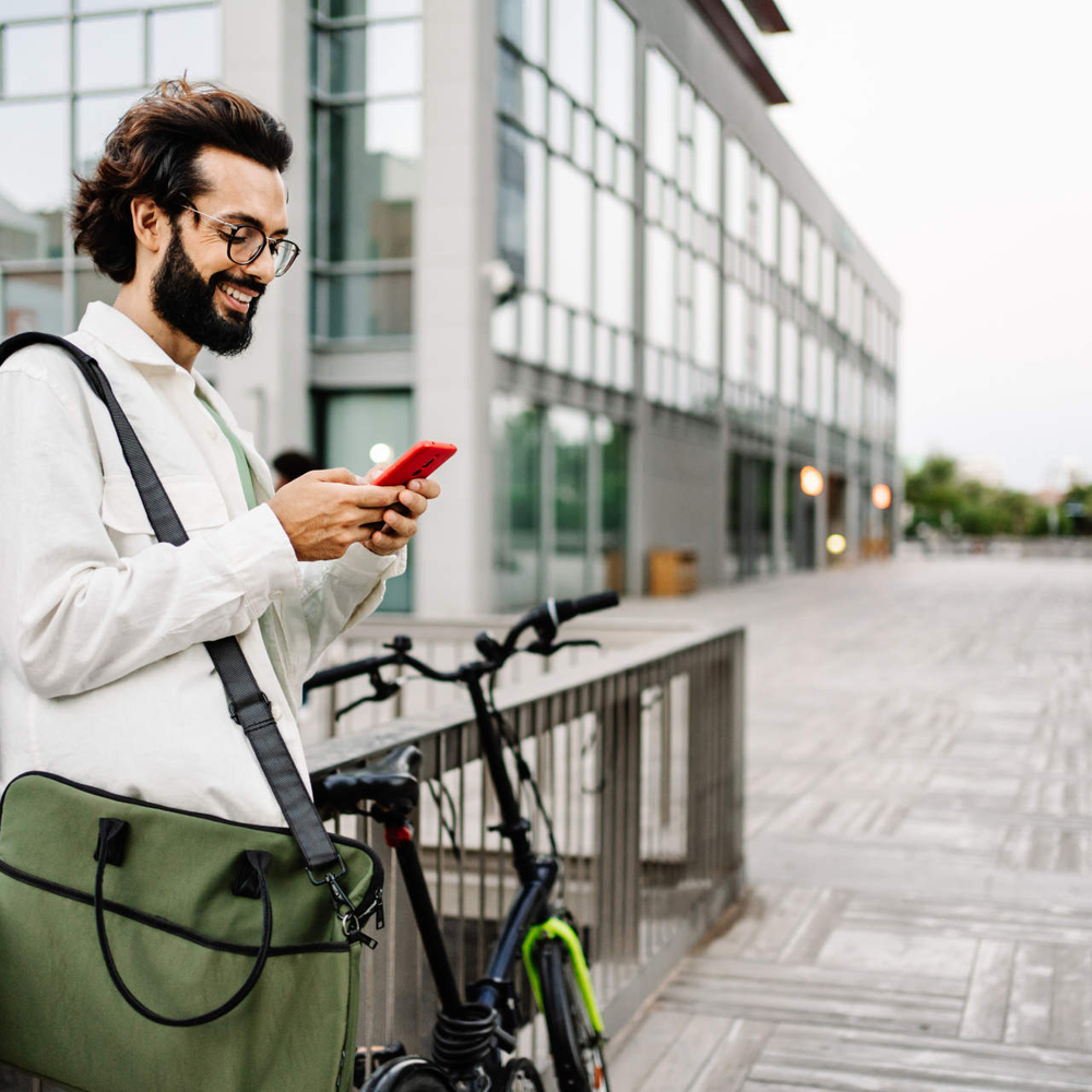 Richtiges Verhalten mit einer Fahrradversicherung Mann steht neben Rad mit Handy in der Hand