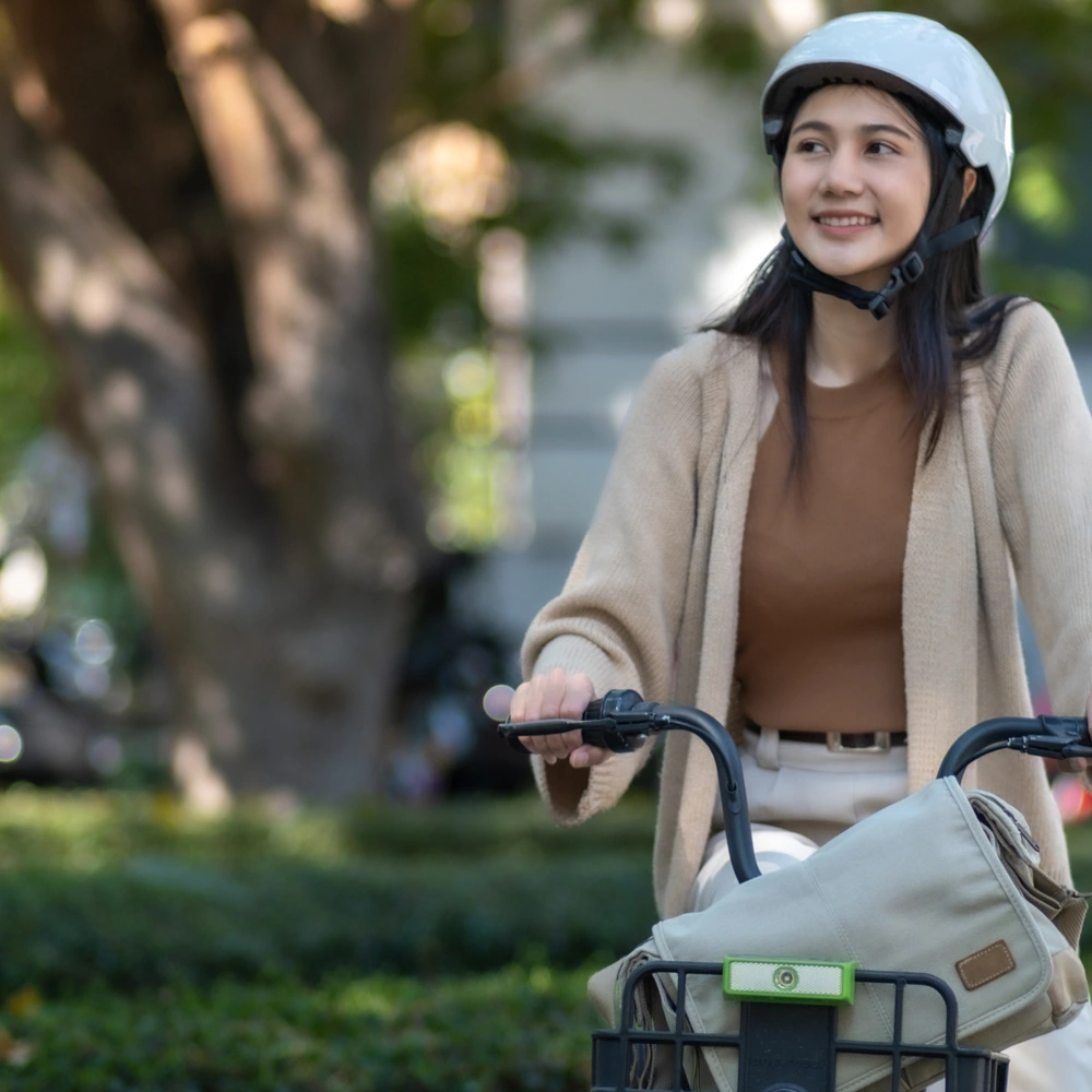 Junge Frau mit Helm auf einem Fahrrad in einem Park, lächelt zufrieden.