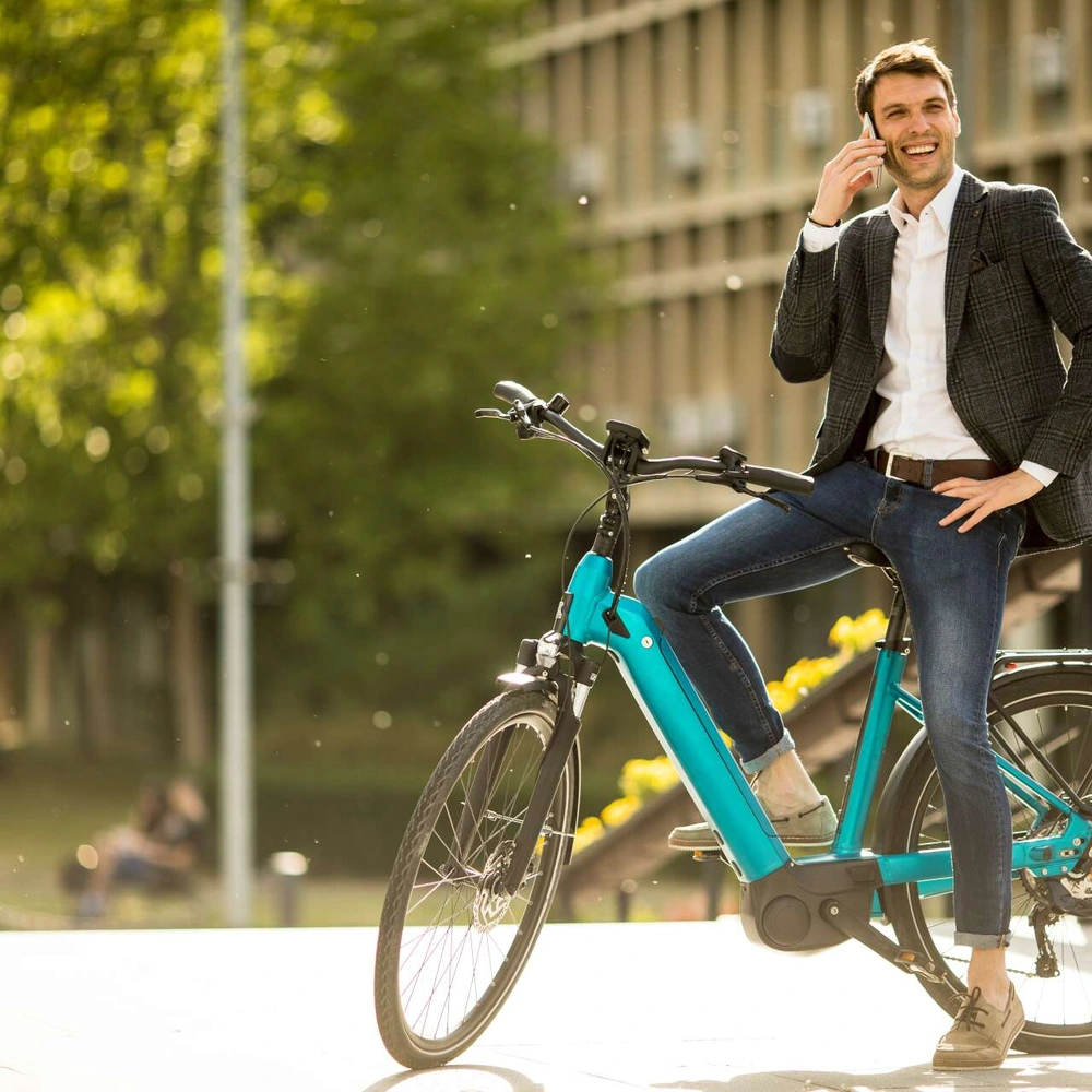 Lächelnder Mann in Anzug telefoniert stehend auf einem E-Bike 