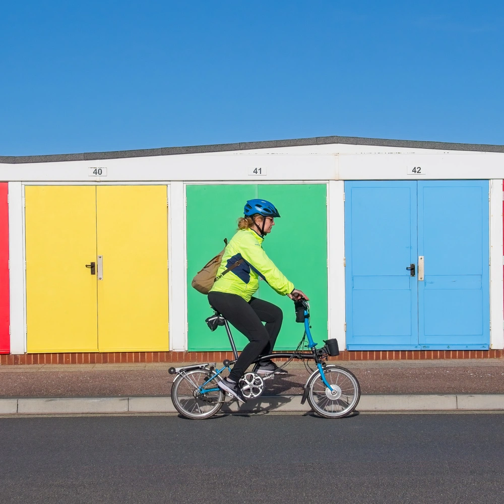 Fahrradfahrerin auf eine Faltrad fährt vor bunten Garagen