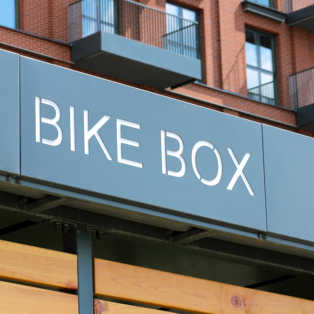 Schild mit der Aufschrift "BIKE BOX" an einer modernen Gebäude-Fassade.