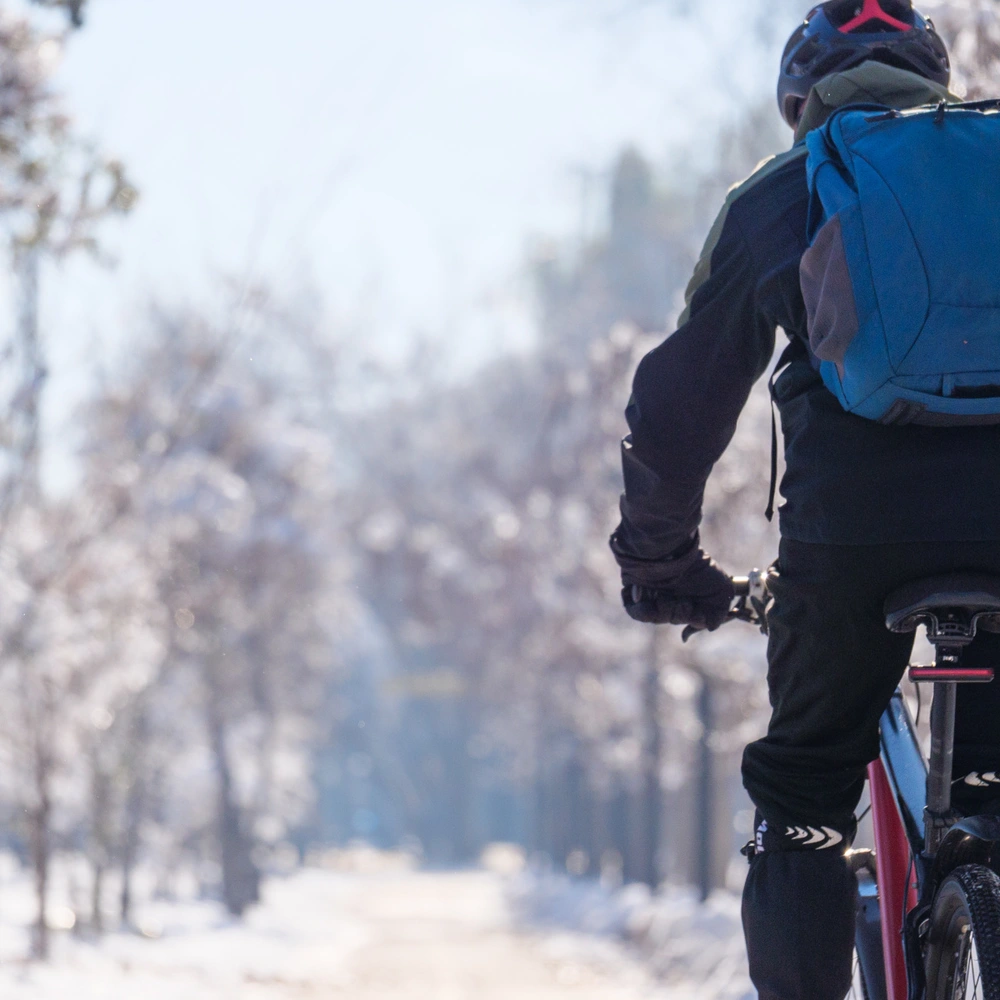Ein Radfahrer fährt auf einem verschneiten Weg zwischen Bäumen.