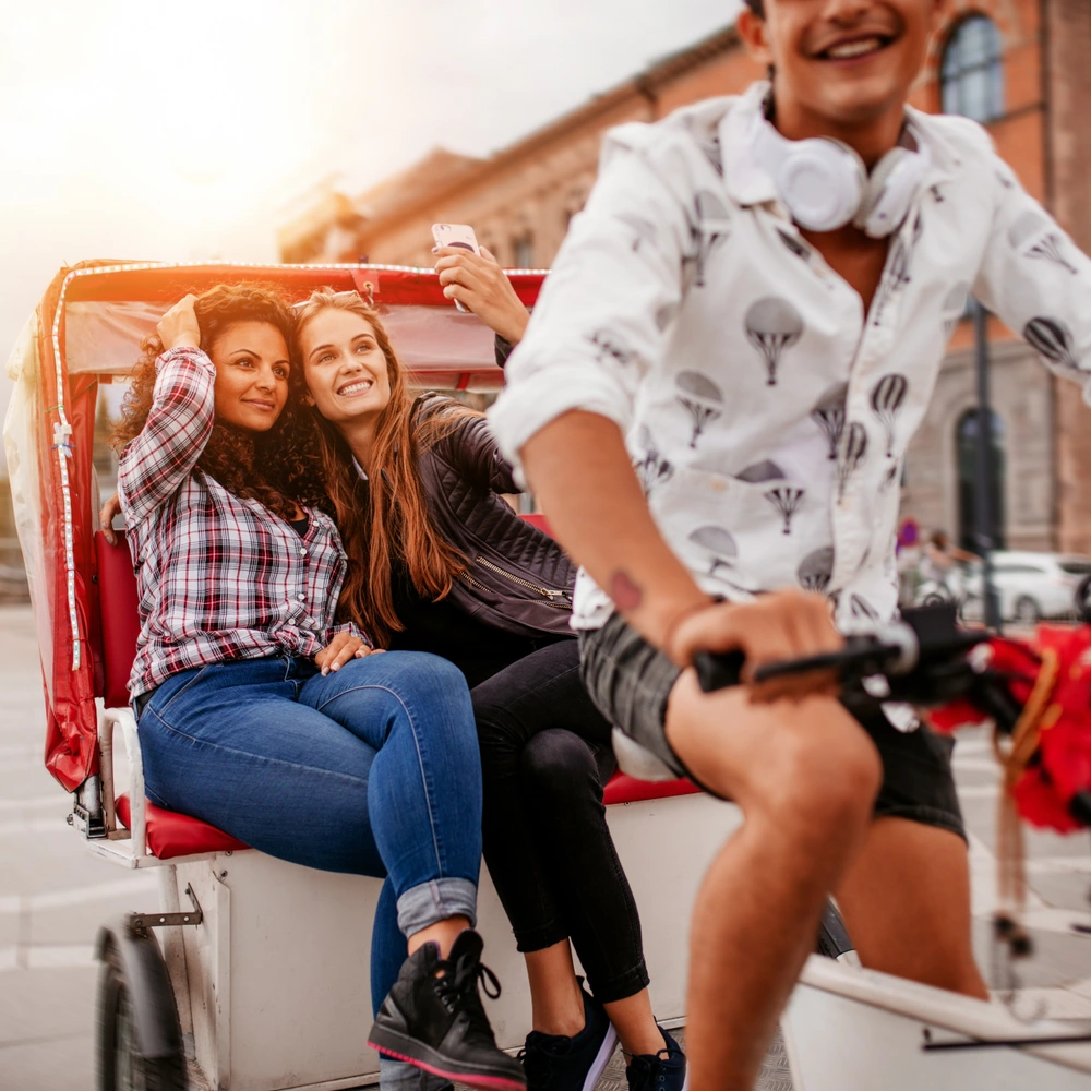 Zwei junge Frauen sitzen entspannt in einer Fahrradrikscha, die von einem Fahrer gesteuert wird