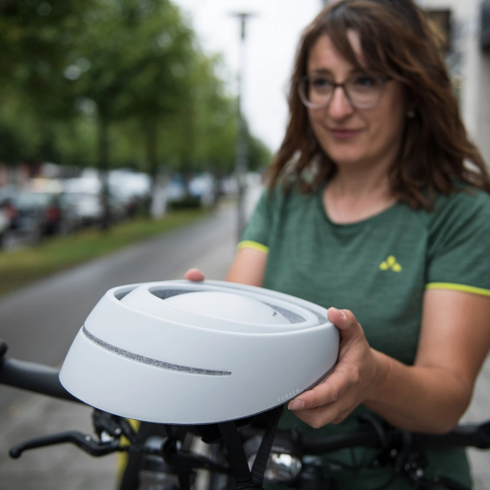 Falthelm des spanischen Herstellers Closca Radfahrerin hält zusammengefalteten Helm von Closca in der Hand.