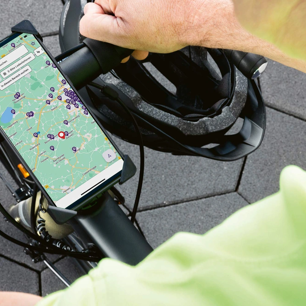 Eine Hand mit einem Smartphone auf einem Fahrradlenker, im Hintergrund ein Helm.