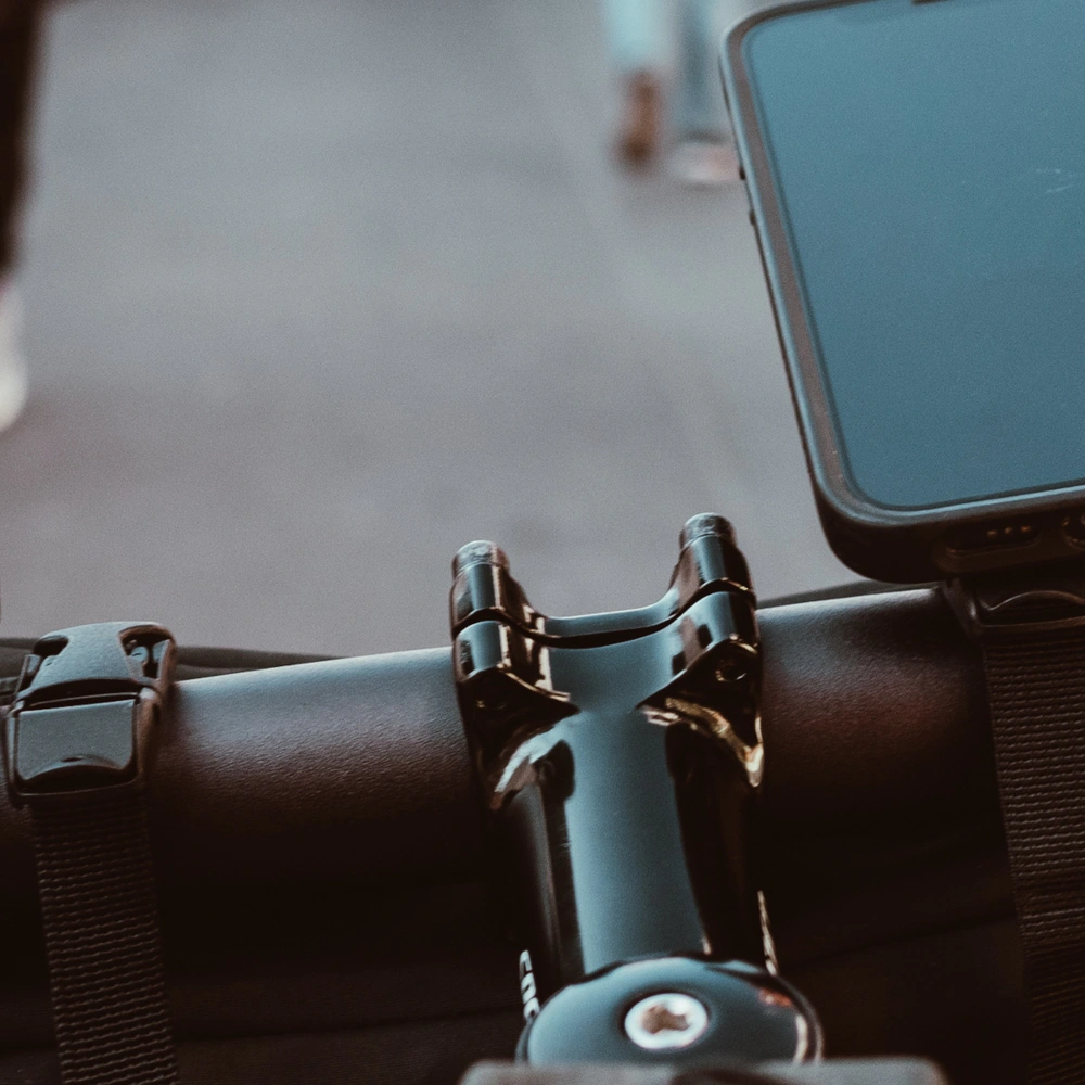 Blick auf den Lenker eines Fahrrads mit einem Smartphonehalter und Fußgängern im Hintergrund.