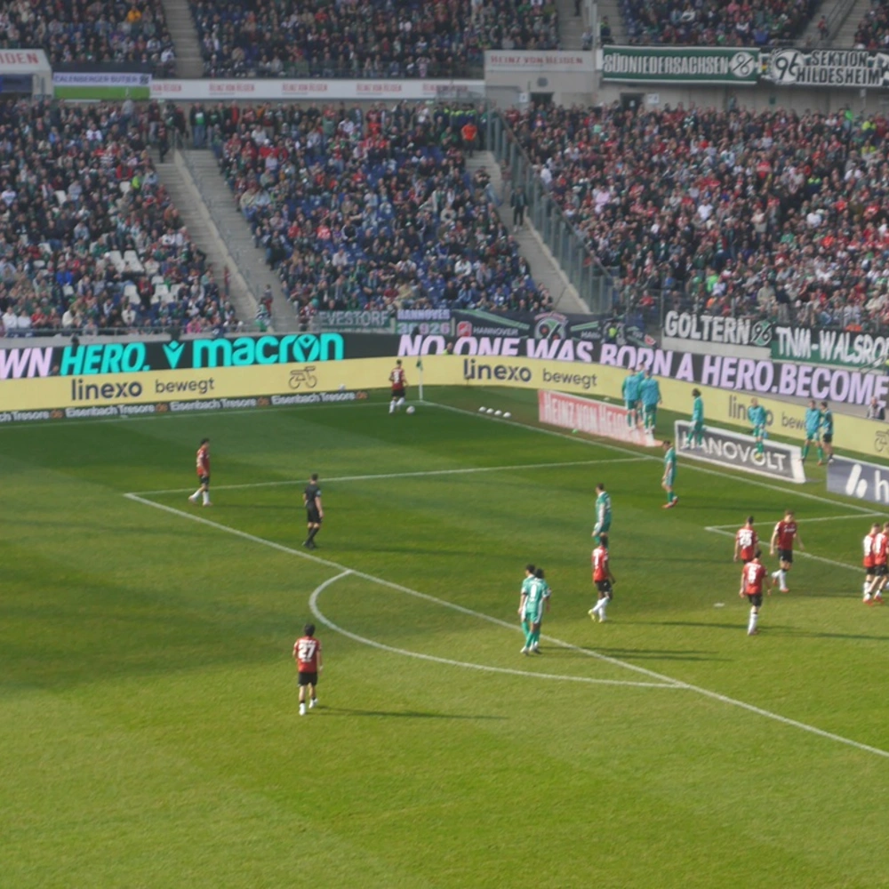 Hannover 96 Fußballspiel im Stadion mit Spielern am Elfmeterpunkt und jubelndem Publikum.