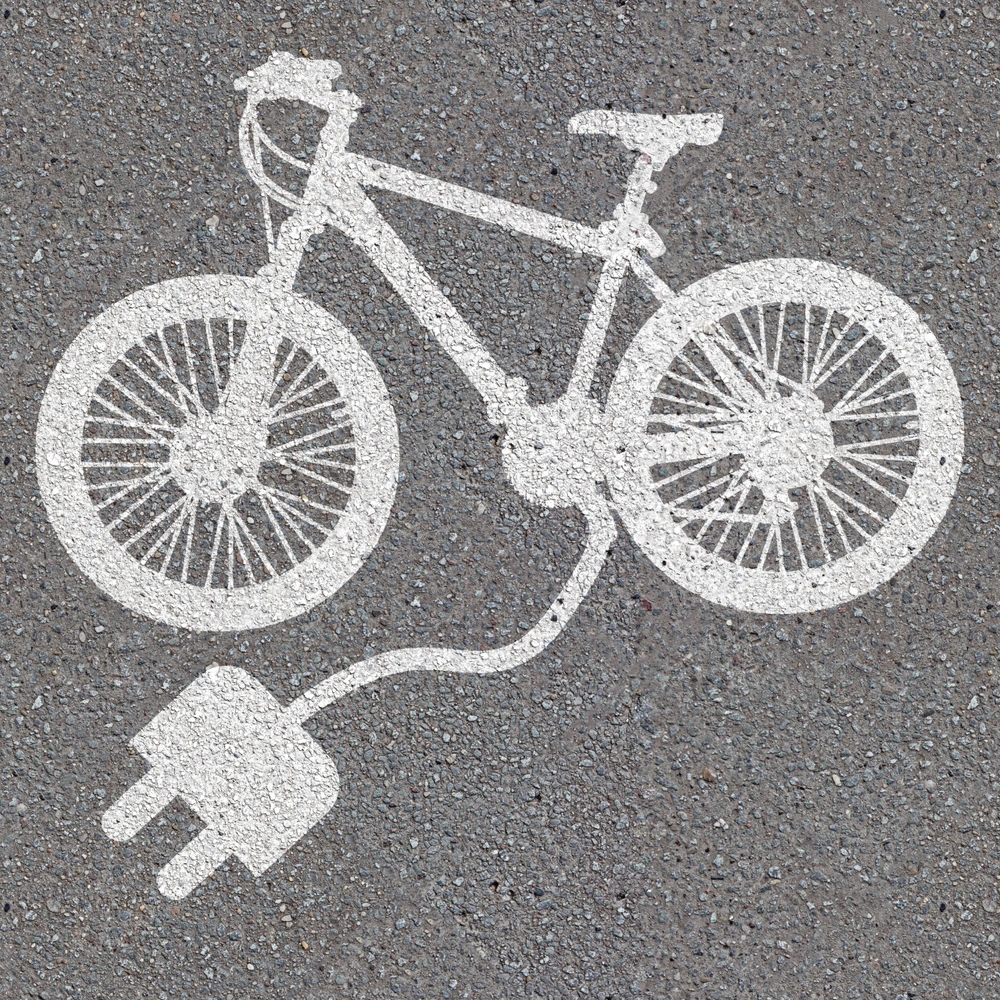 Weißes E-Bike-Symbol auf grauem Asphalt mit einem Steckdosenanschluss
