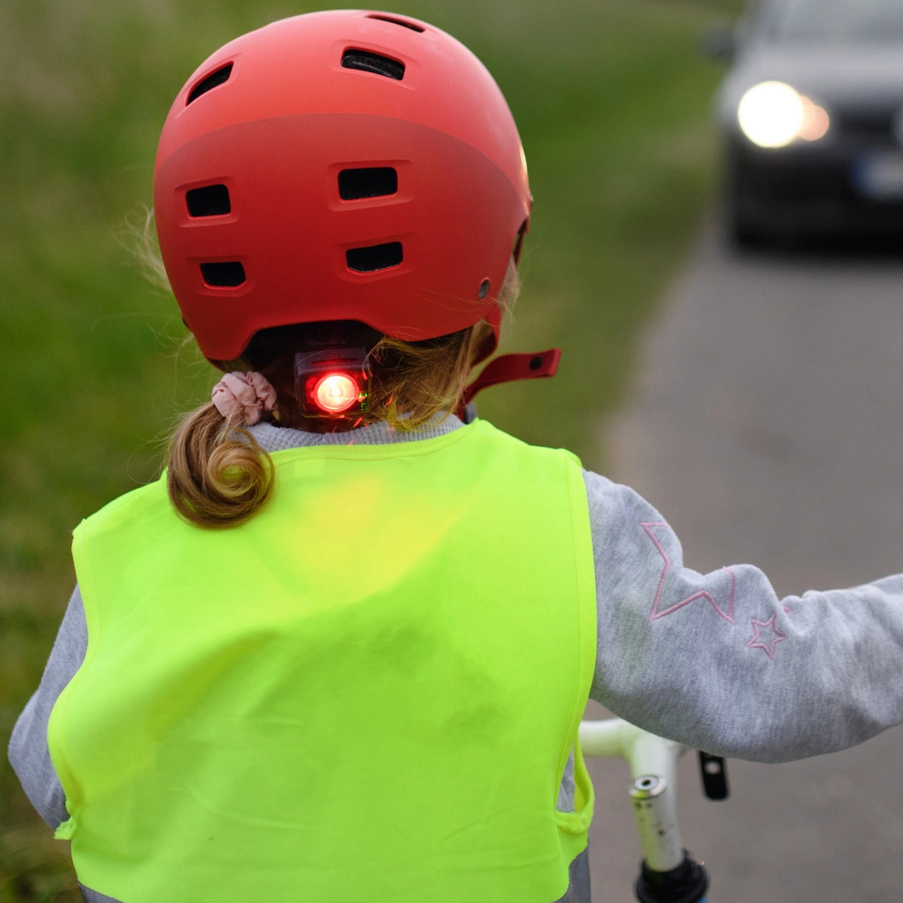 Ein Kind mit rotem Helm und reflektierender Weste fährt mit dem Fahrrad auf der Straße.