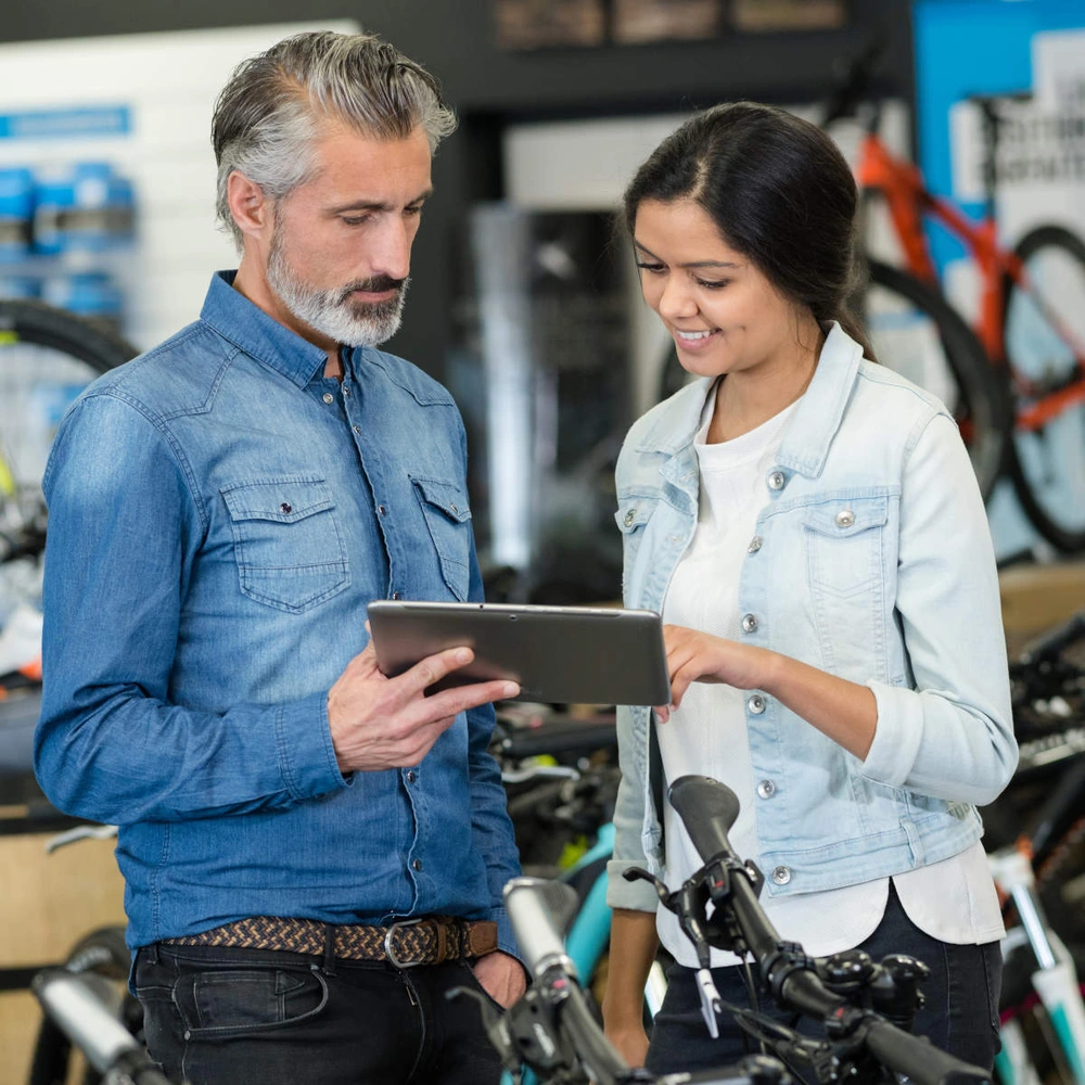 Mann und Frau stehen in Fahrradgeschäft und gucken auf Tablet.
