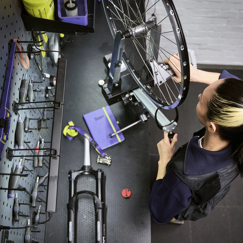 Eine Person repariert ein Fahrradrad an einem Arbeitstisch, umgeben von Werkzeugen.