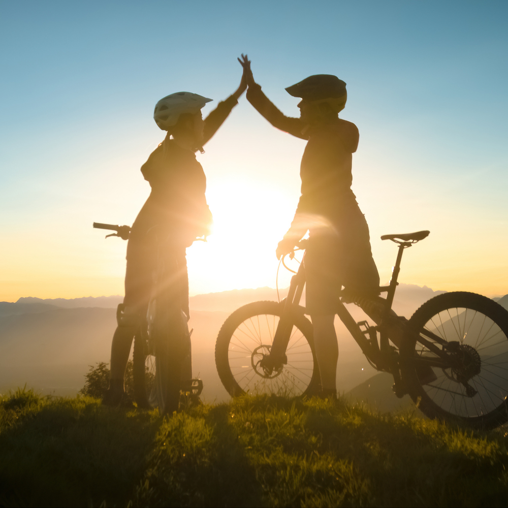 Mercedes E-Bike News: Formel-1-Feeling E-Bikes Zwei Frauen schlagen ein im Sonnenuntergang auf dem Fahrrad in den Bergen