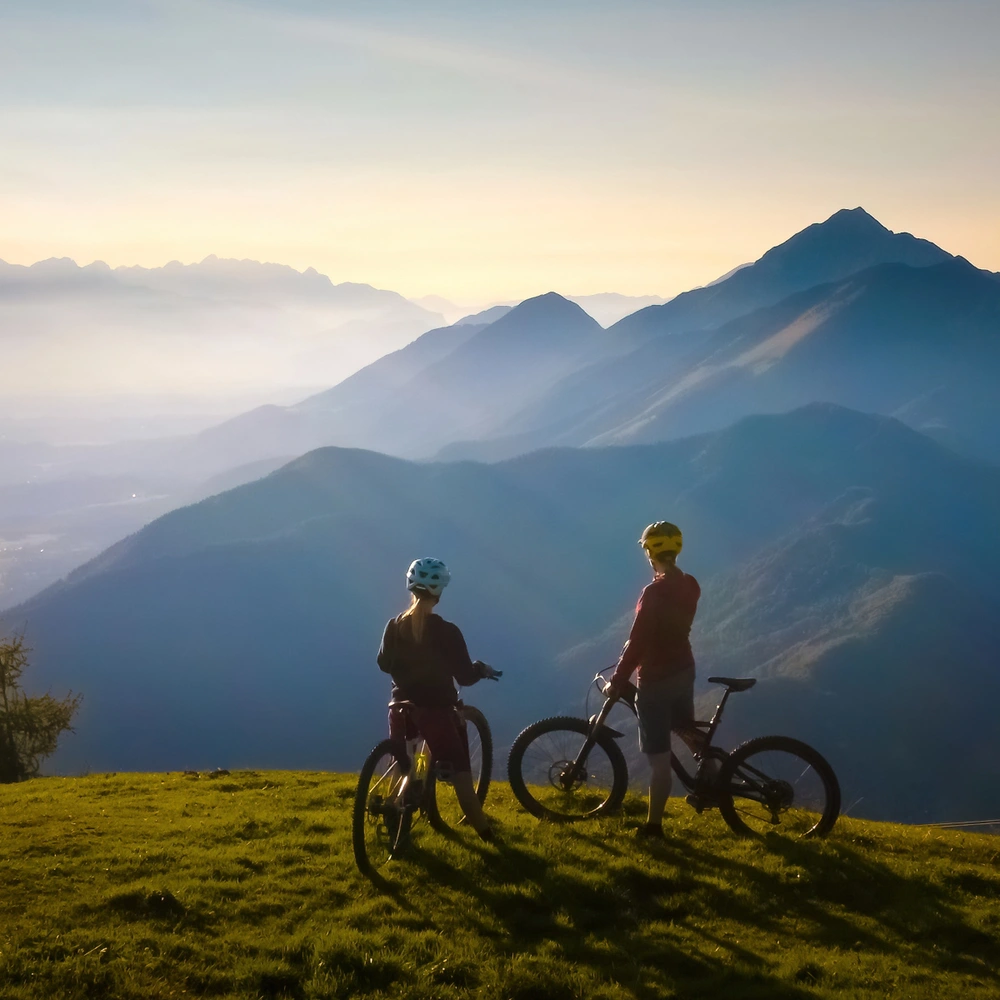 Zwei Fahrradfahrerinnen stehen auf einem Berg und schauen in die Ferne