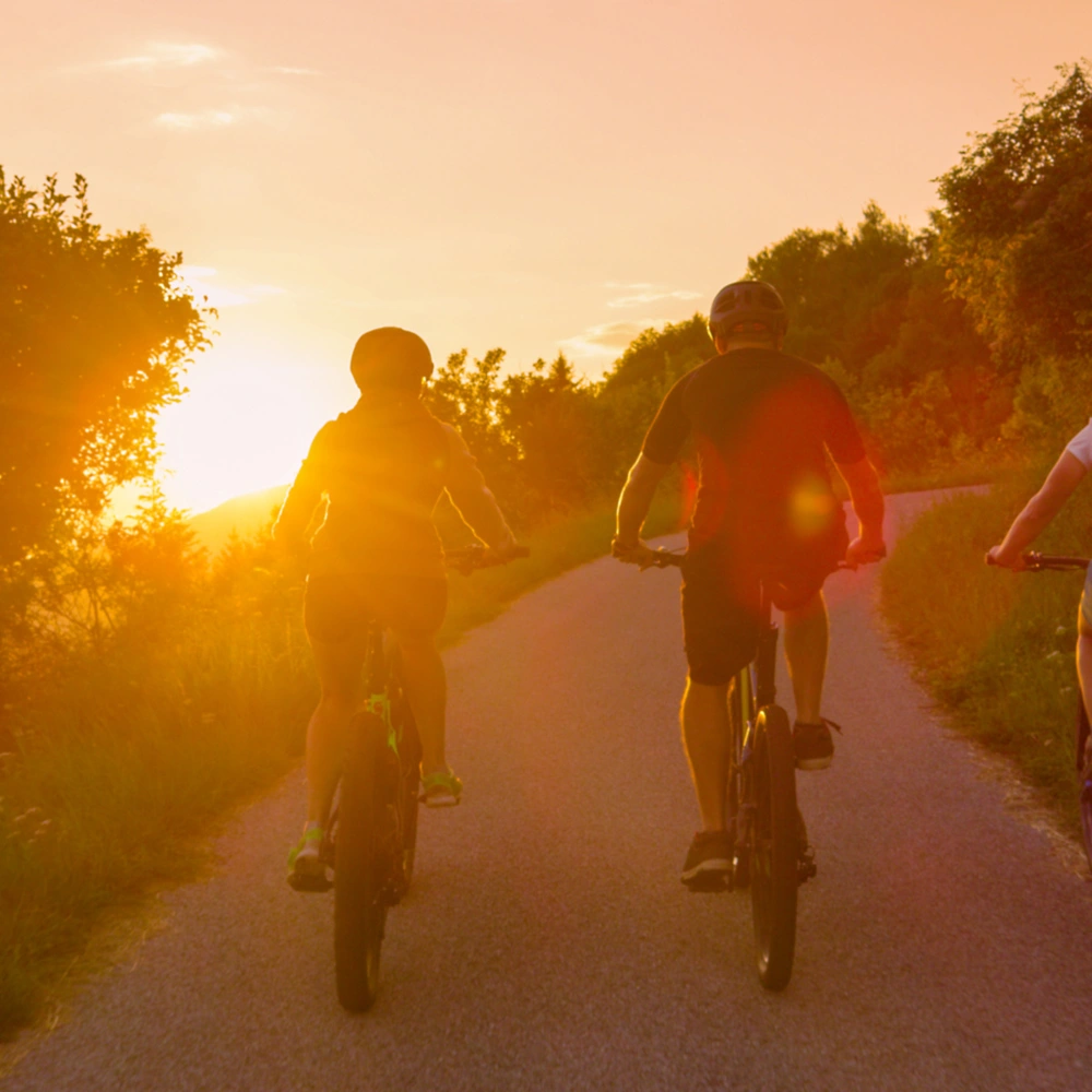 Drei Personen fahren mit E-Bikes im Sonnenuntergang