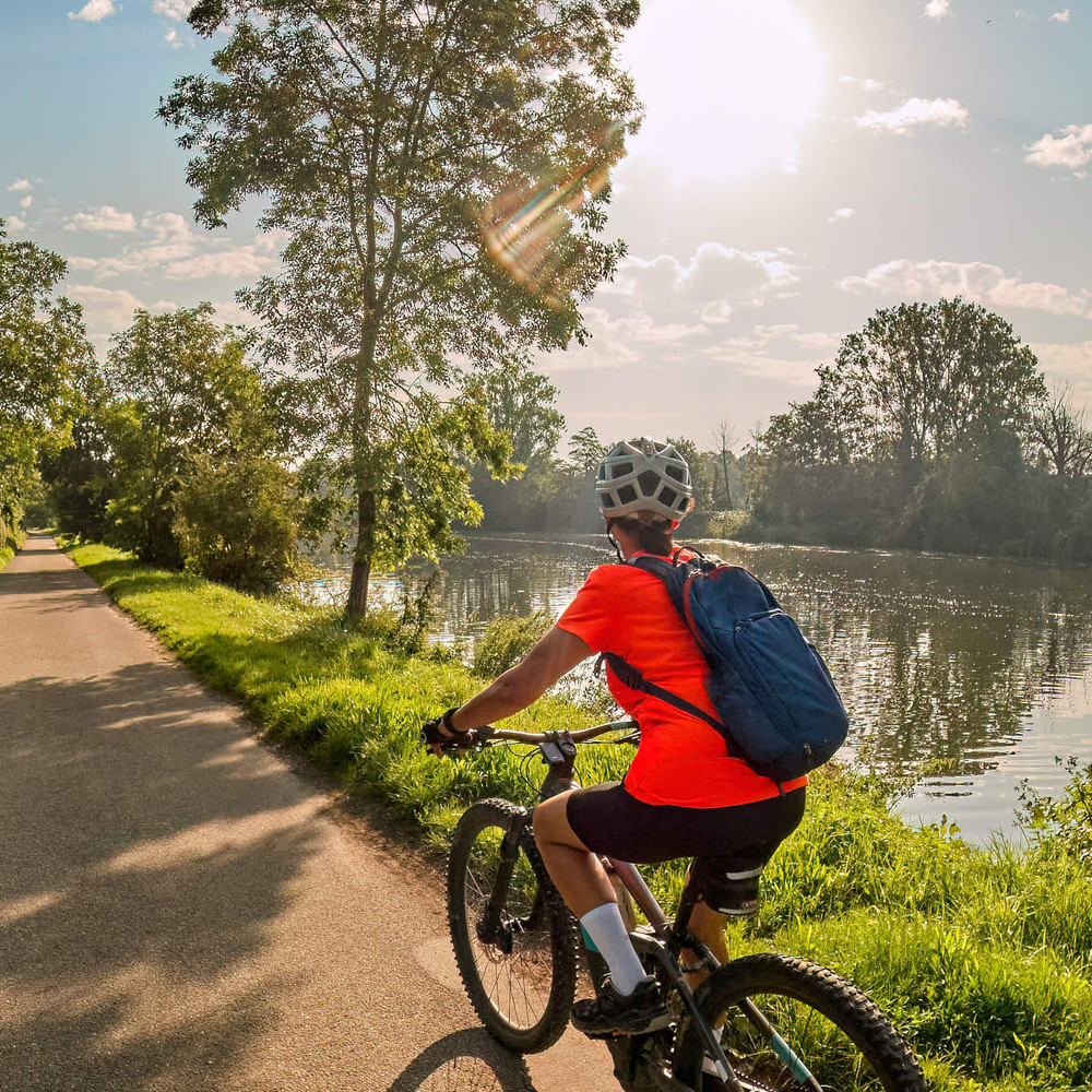 Entdecke mit Rockrider E-Bikes die innovativen Bikes von Decathlon Frau fährt an einem Flussufer mit einem E-Bike entlang